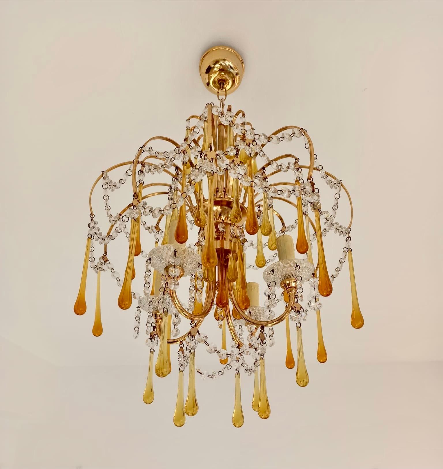 A beautiful original vintage Italian chandelier designed by Paolo Venini in the 1960s in brass and Murano glass, this pendant is surmounted at the top by a crown of curved brass rods with amber glass drops suspended at the ends.
The structure is