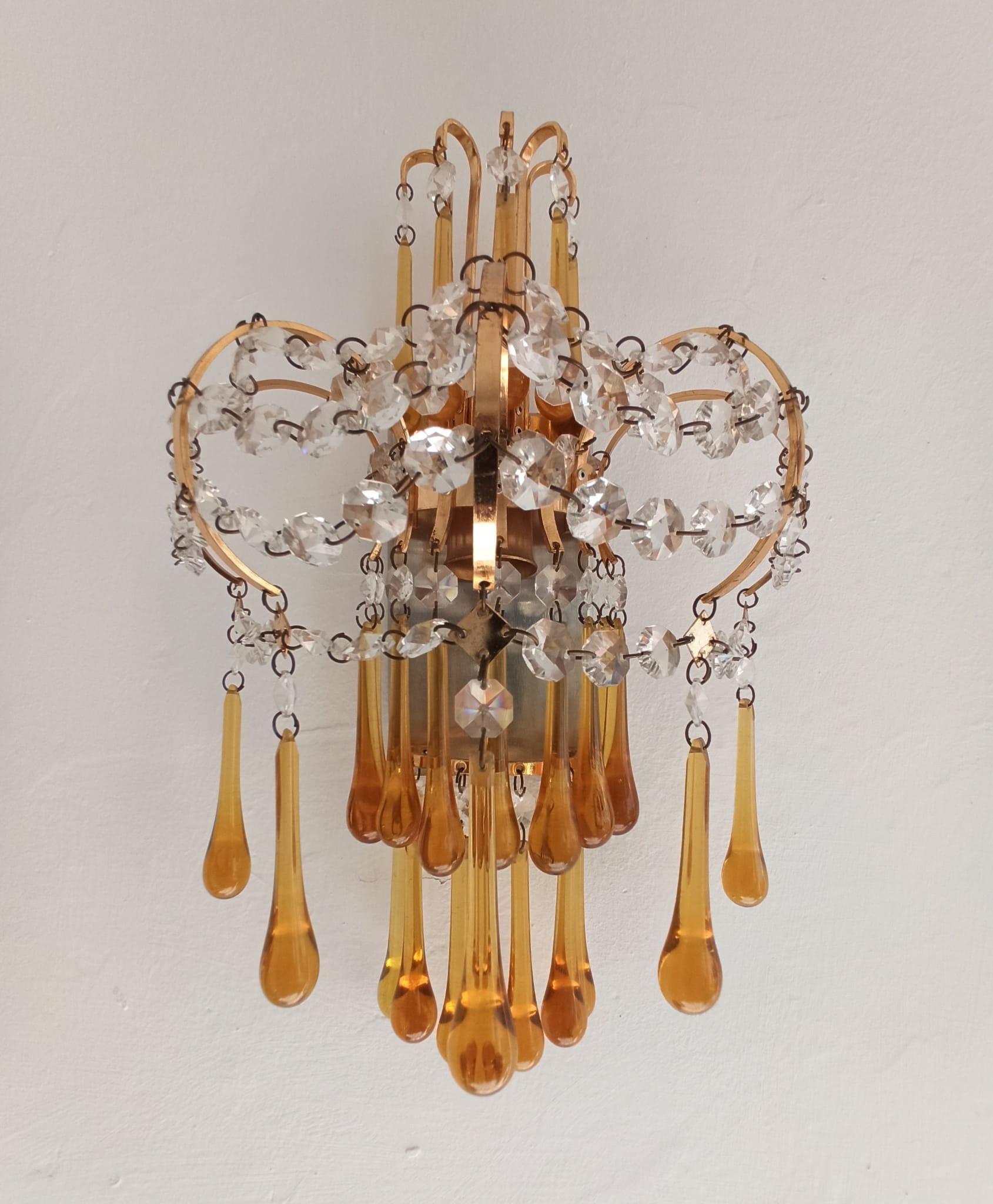A beautiful original vintage Italian pair of wall lamps designed by Paolo Venini in the 1960s in brass and Murano glass surmounted at the top by a half moon crown of curved brass rods with amber glass drops suspended at the ends.
The structure is