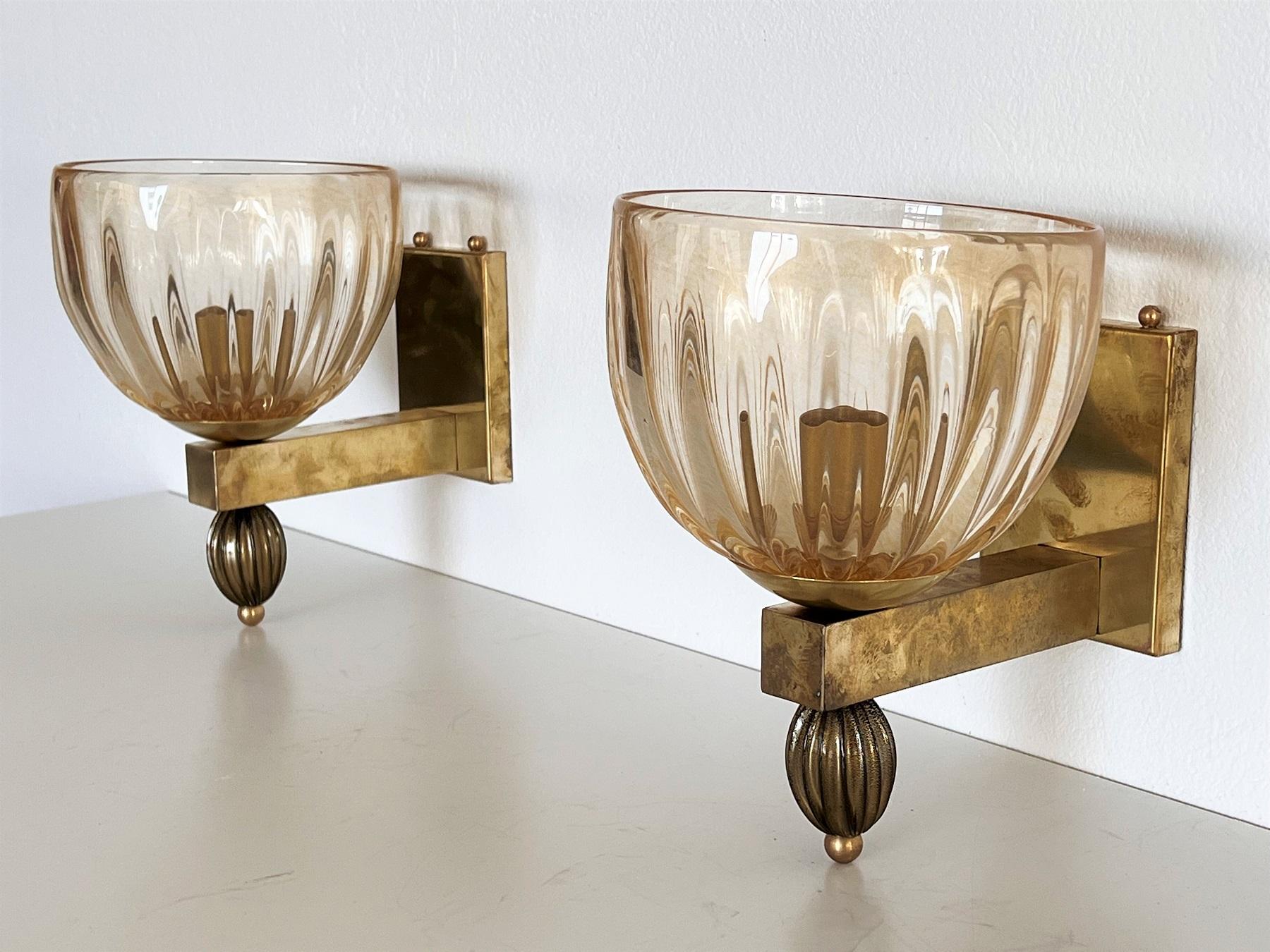 Beautiful set of two gorgeous brass wall lamps made of strong brass base and light amber-transparent Murano glasses with golden shimmer/glitter inside the glass. 
On the bottom of the sconces are large fluted beads, which are also made by hand from