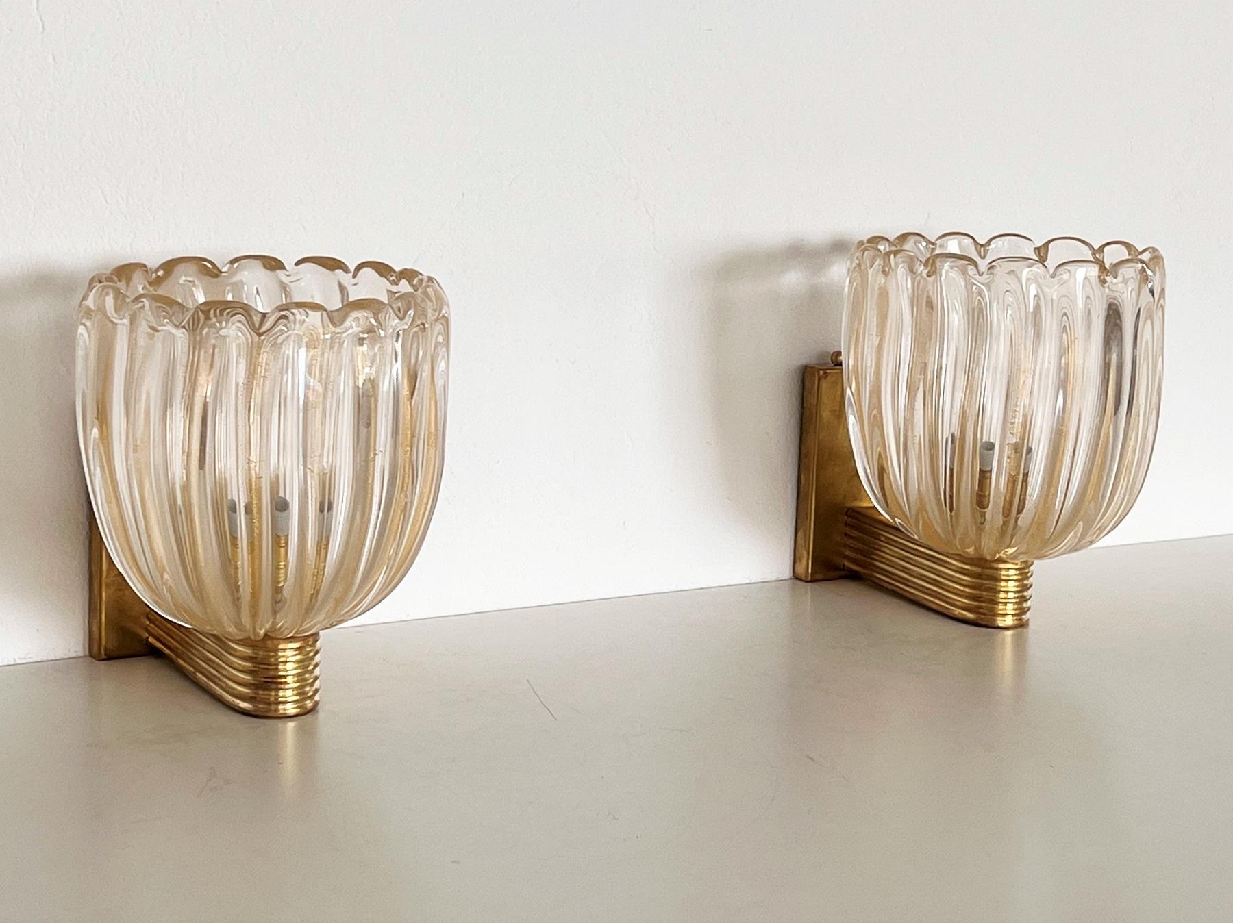 Beautiful set of two gorgeous brass wall lamps made of strong brass base and transparent thick Murano glasses with golden shimmer/glitter inside the glass. Art Deco style.
The beautiful hand-crafted glasses have a slight wave shape, please look