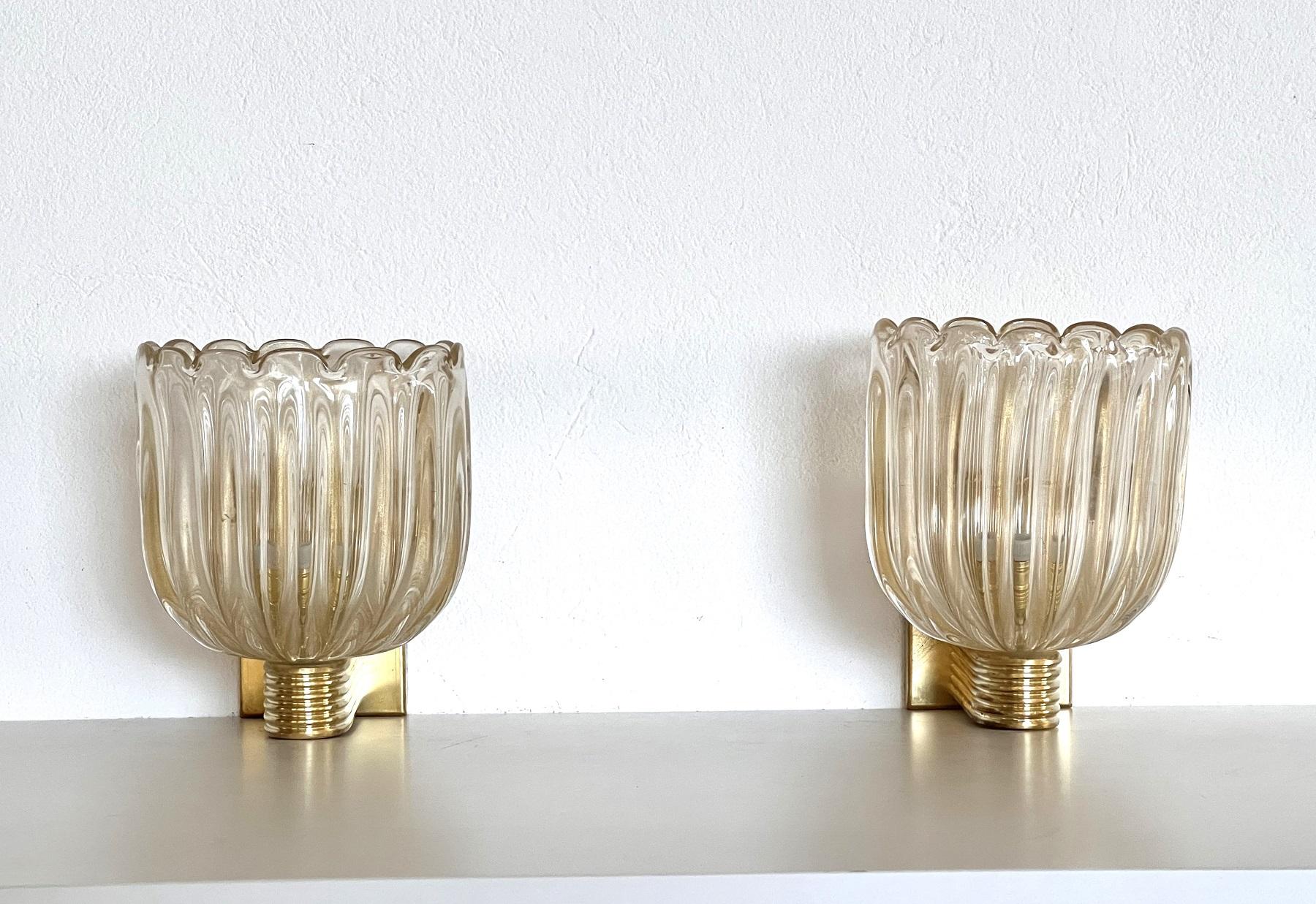 Beautiful set of two gorgeous brass wall lamps made of strong brass base and transparent thick Murano glasses with golden shimmer/glitter inside the glass. 
Art Deco style.
The beautiful hand-crafted glasses have a slight wave shape, please look