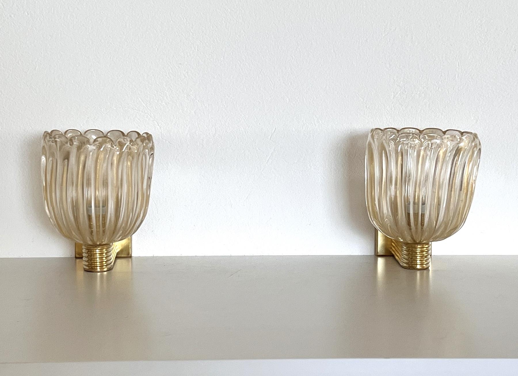 Beautiful set of two gorgeous brass wall lamps made of strong brass base and transparent thick Murano glasses with golden shimmer/glitter inside the glass. Art Deco style.
The beautiful hand-crafted glasses have a slight wave shape, please look