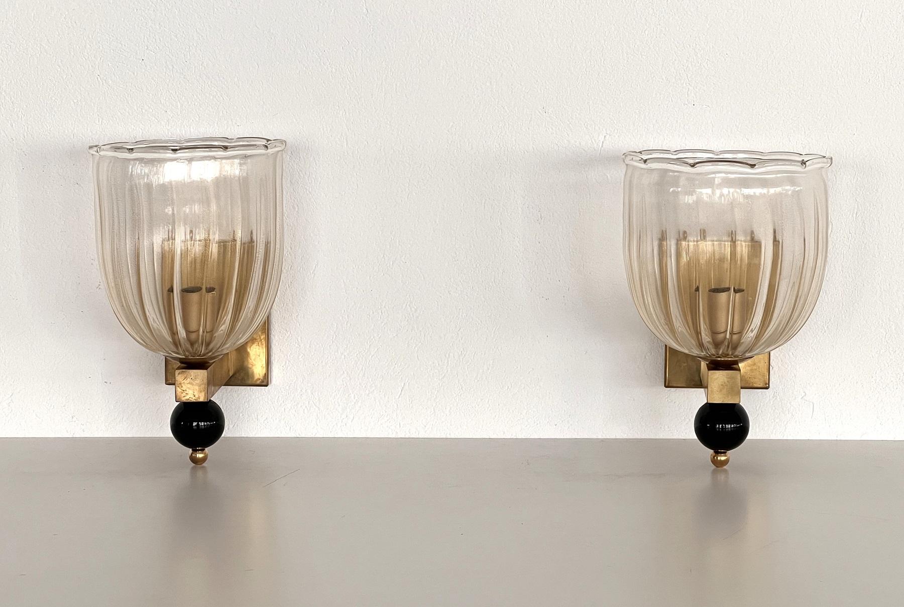 Beautiful set of two gorgeous wall lamps made of light transparent Murano glasses with golden shimmer/glitter inside the glass and strong brass base.
At the bottom of the wall lamps are large glass balls, also handmade from black Murano glass. They