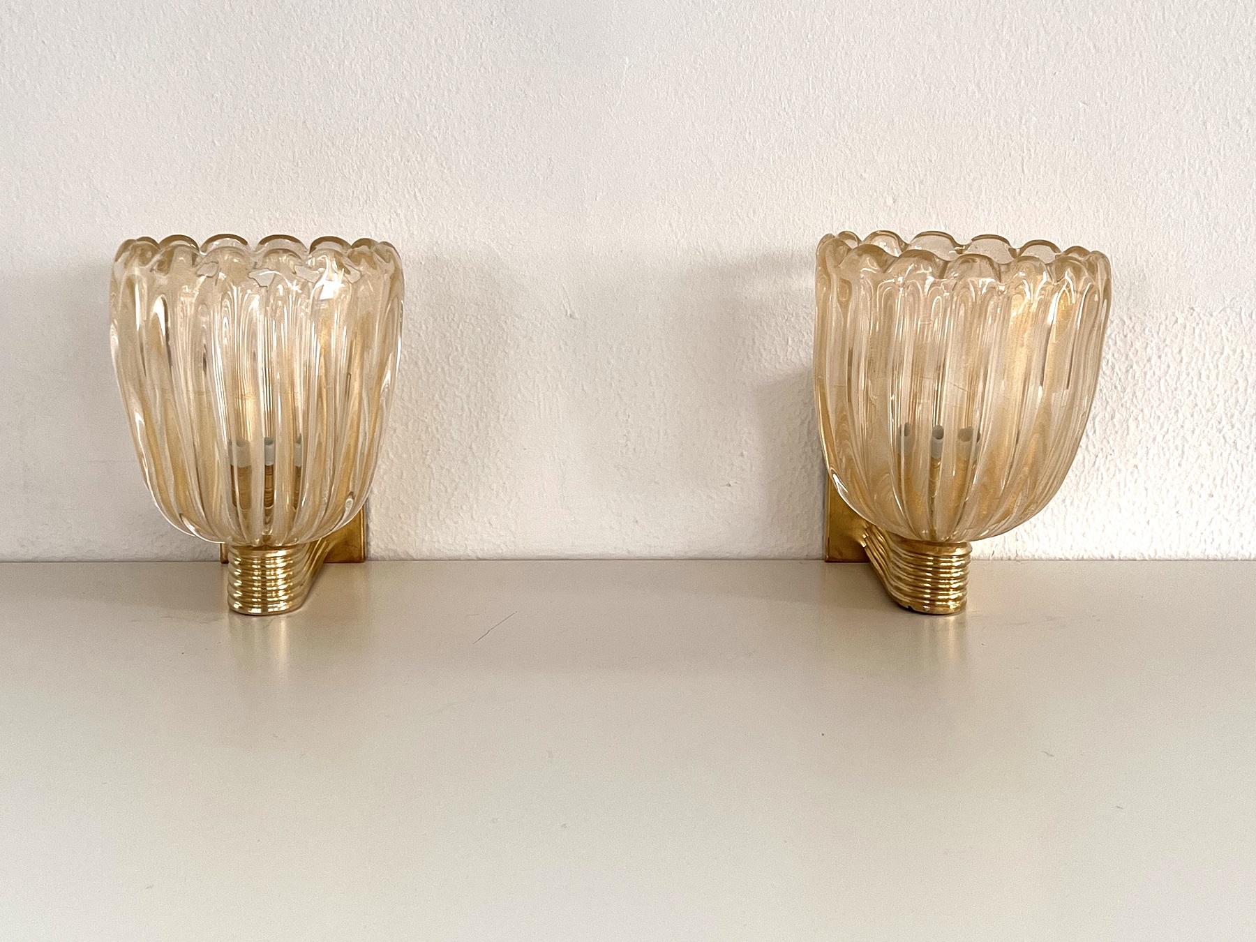 Beautiful set of two gorgeous brass wall lamps made of strong brass base and transparent thick Murano glasses with golden shimmer/glitter inside the glass. Art Deco style.
The beautiful hand-crafted glasses have a slight wave shape and few small air