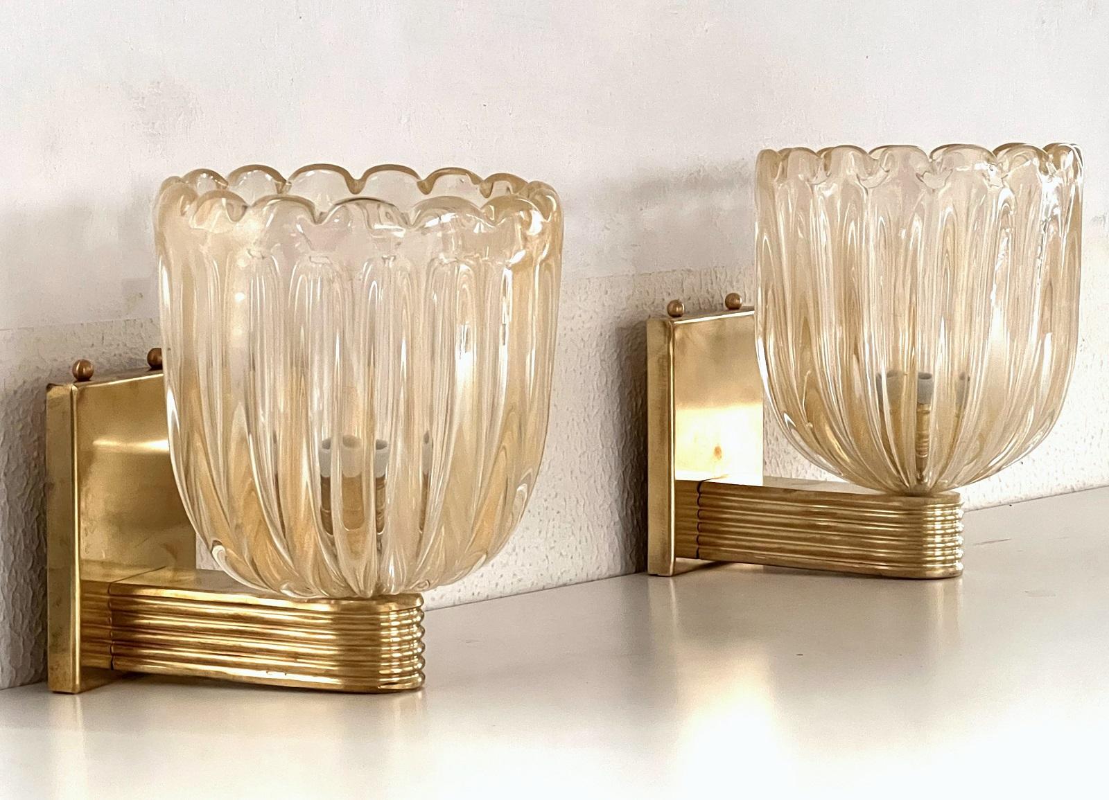 Beautiful set of two gorgeous brass wall lamps made of strong brass base and transparent thick Murano glasses with golden shimmer/glitter inside the glass. Art Deco style.
The beautiful hand-crafted glasses have a slight wave shape and few small air