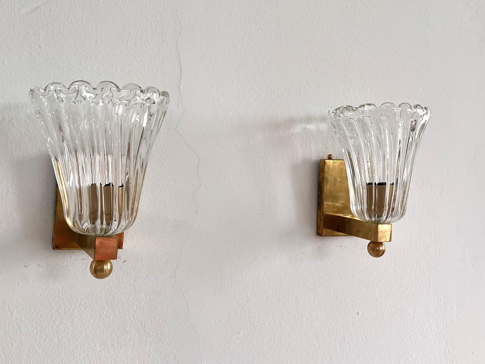 Schönes Set von zwei wunderschönen Wandlampen aus starken transparenten dicken Murano-Gläsern und starken Messing Basis gemacht. Art-Déco-Stil. Wunderschön mit der Messingkugel an der Unterseite der Lampe
Die schönen handgefertigten Gläser haben
