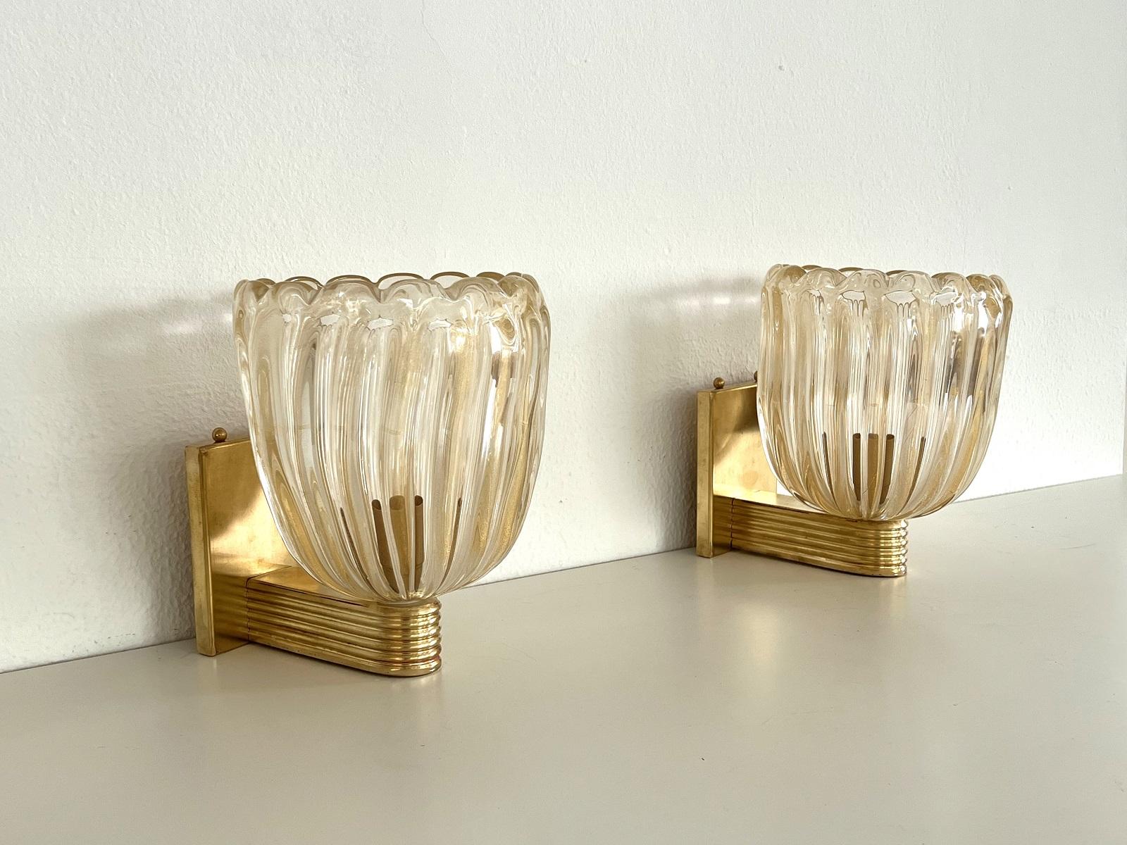 Wunderschönes Set aus zwei prächtigen Messing-Wandlampen mit starkem Messingsockel und transparenten, dicken Murano-Gläsern mit goldenem Schimmer/Glitter im Inneren des Glases. Art-Déco-Stil.
Die schönen handgefertigten Gläser haben eine leichte