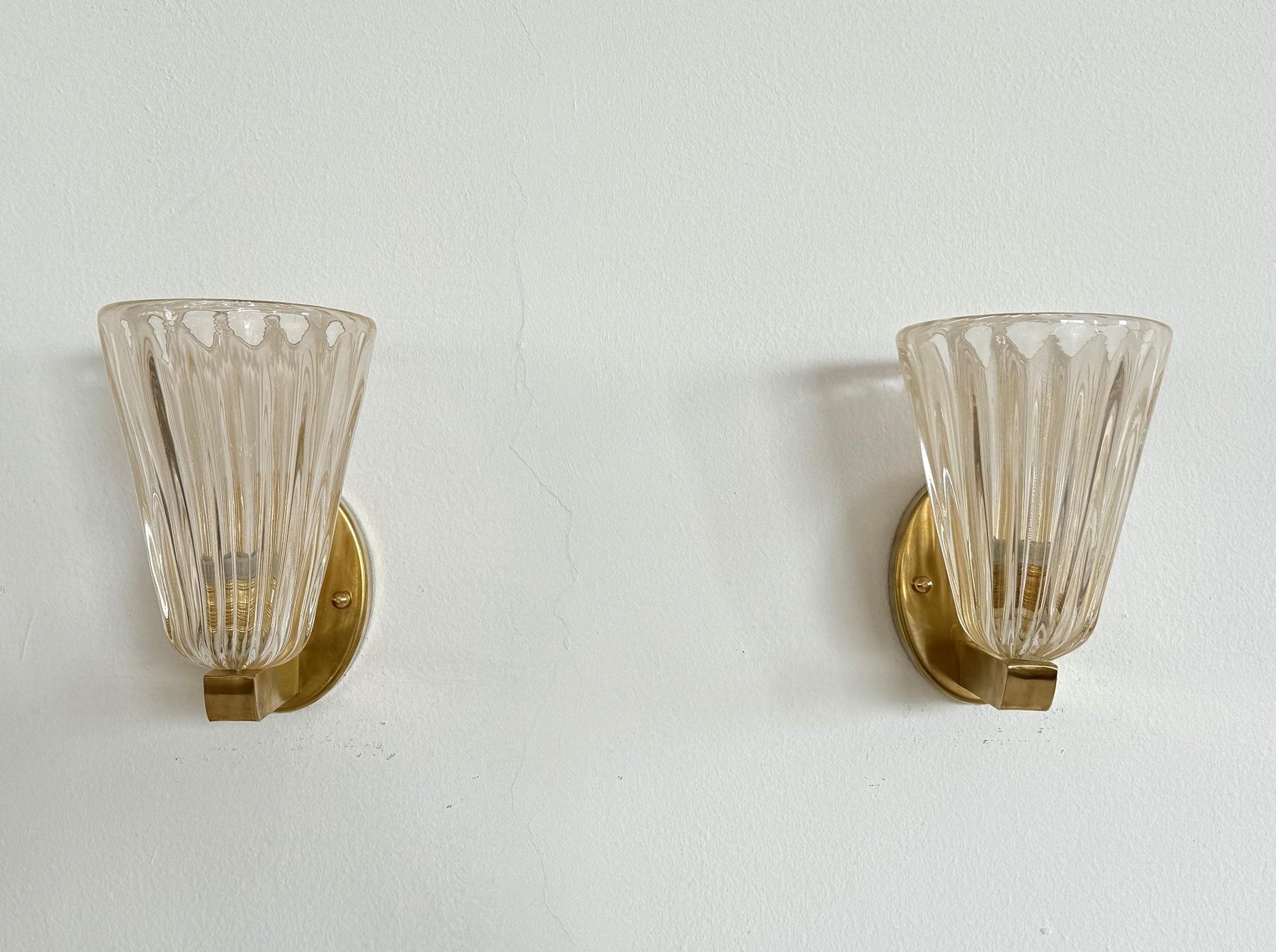 Beautiful set of two gorgeous brass wall lamps made of strong brass base and light amber colored Murano glasses with golden shimmer/glitter inside the glass. Art Deco style.
The beautiful hand-crafted glasses have a slight wave shape, please look