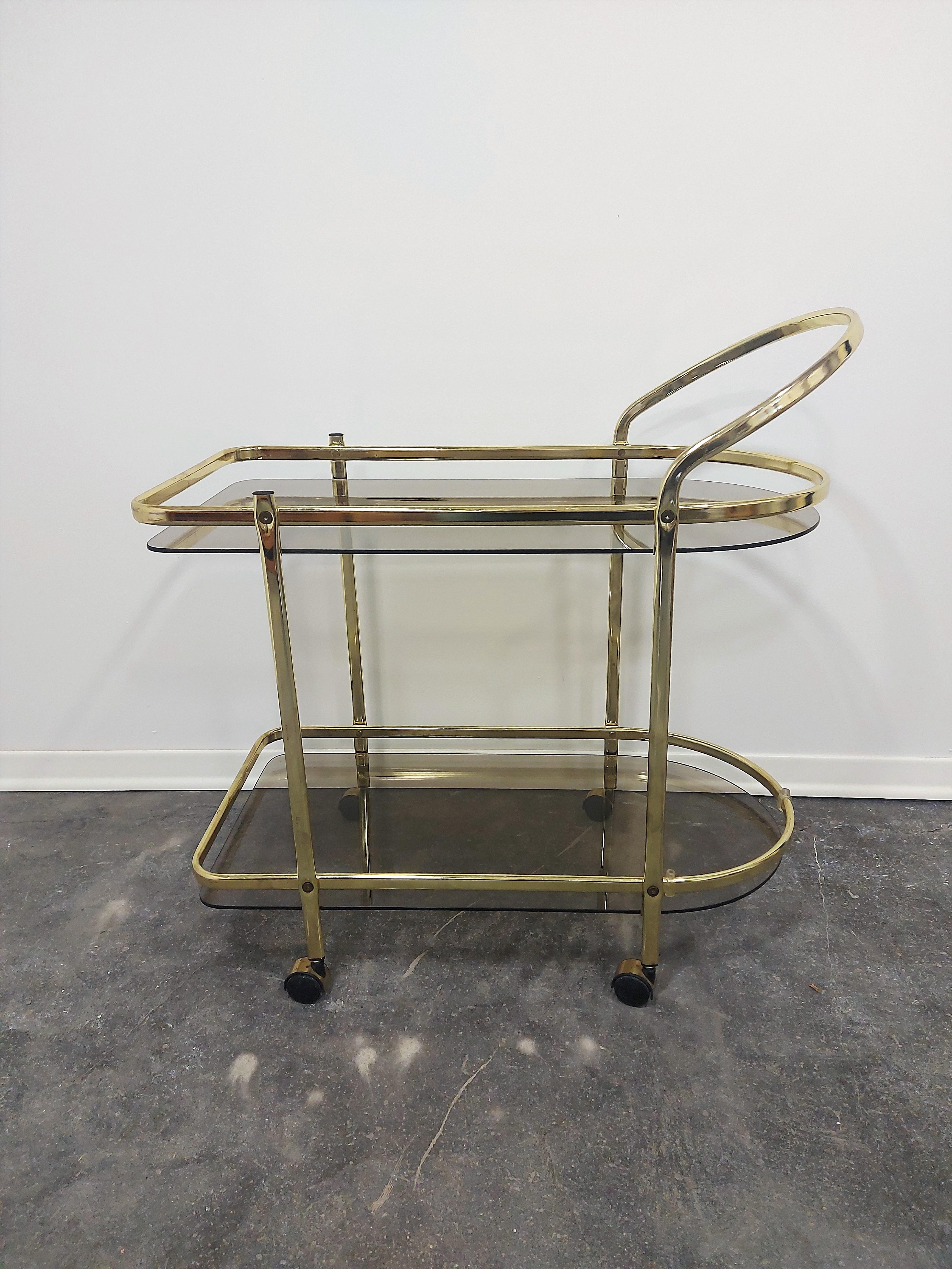 Italian Brass and Smoked glass Bar Cart, 1960s

Perfect in that upscale home with chic design. 

Two tiered for storage. 

Wheel from room to room for your convenience.

H-76,50 cm (1 tier-12,50 cm, 2 tier-55,50 cm) , W-74,50 cm, D-41 cm.