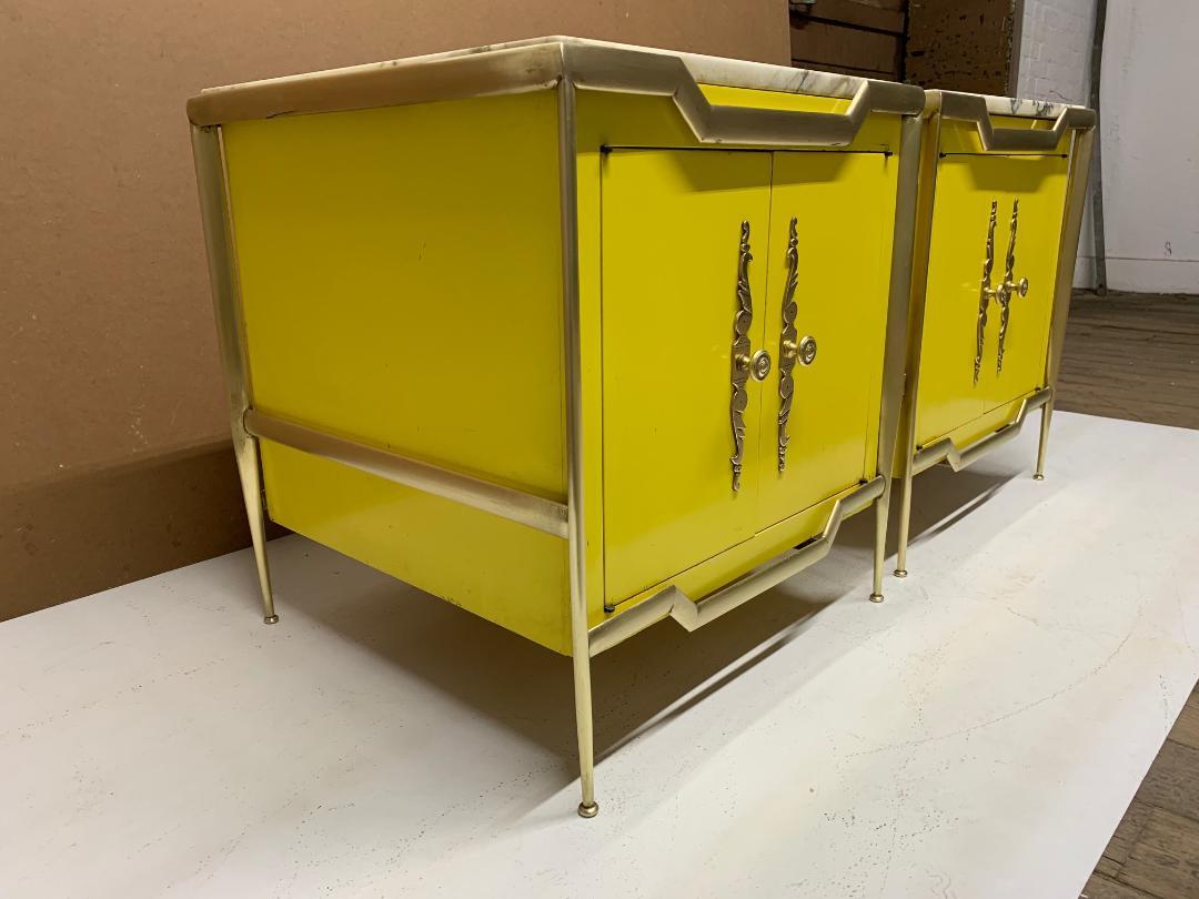 Pair of Italian brass cabinets with marble tops. The cabinets are wood with a yellow painted finish. Has brass frames and decorative brass hardware with an adjustable glass shelf inside. Style of Tommi Parzinger.  