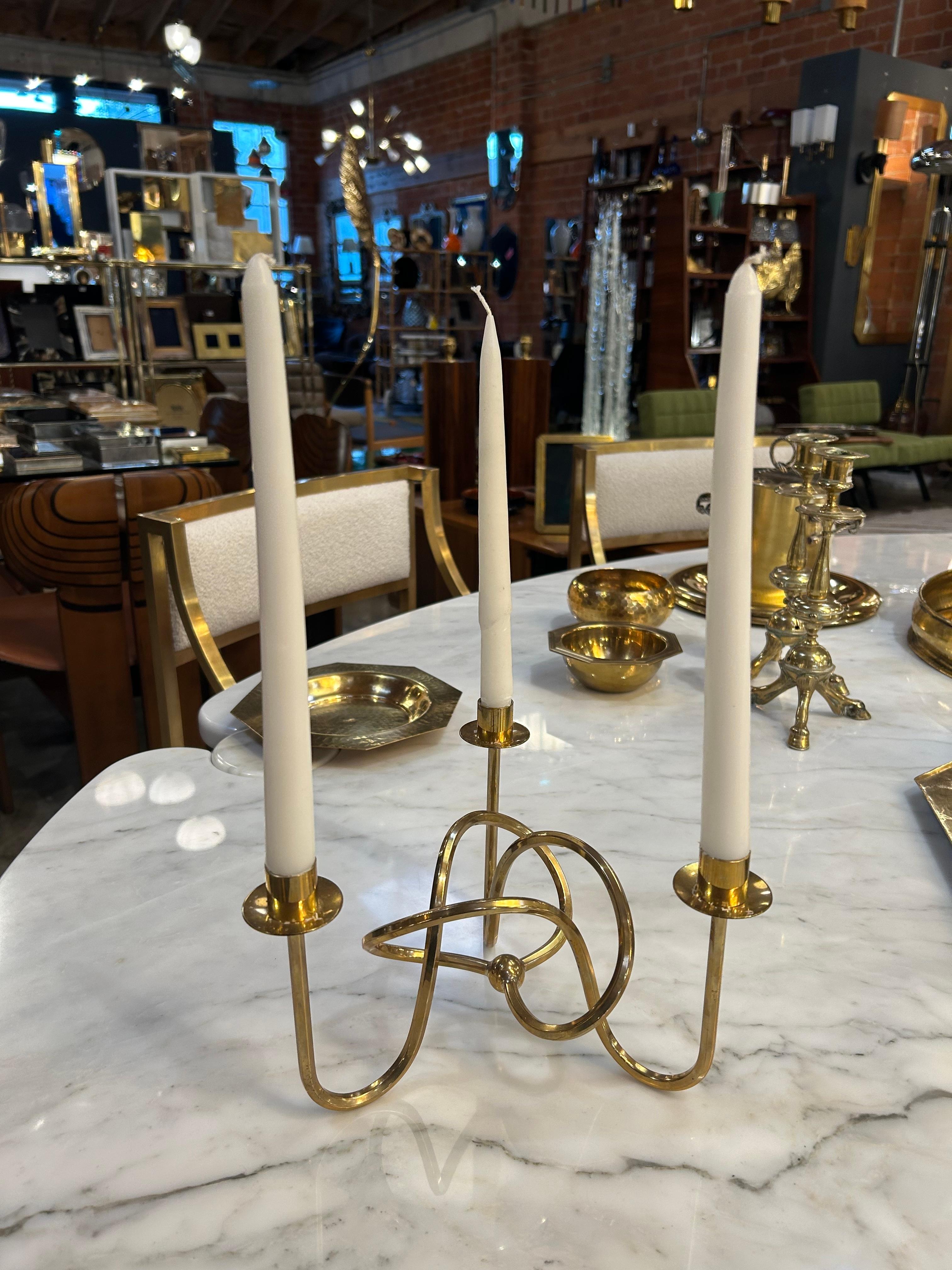 Elevate your space with this exquisite pair of Italian three-arm candelabras. Each piece features a sculptural, looped brass frame that gracefully supports three taper candles, creating an enchanting interplay of curves and light. The polished