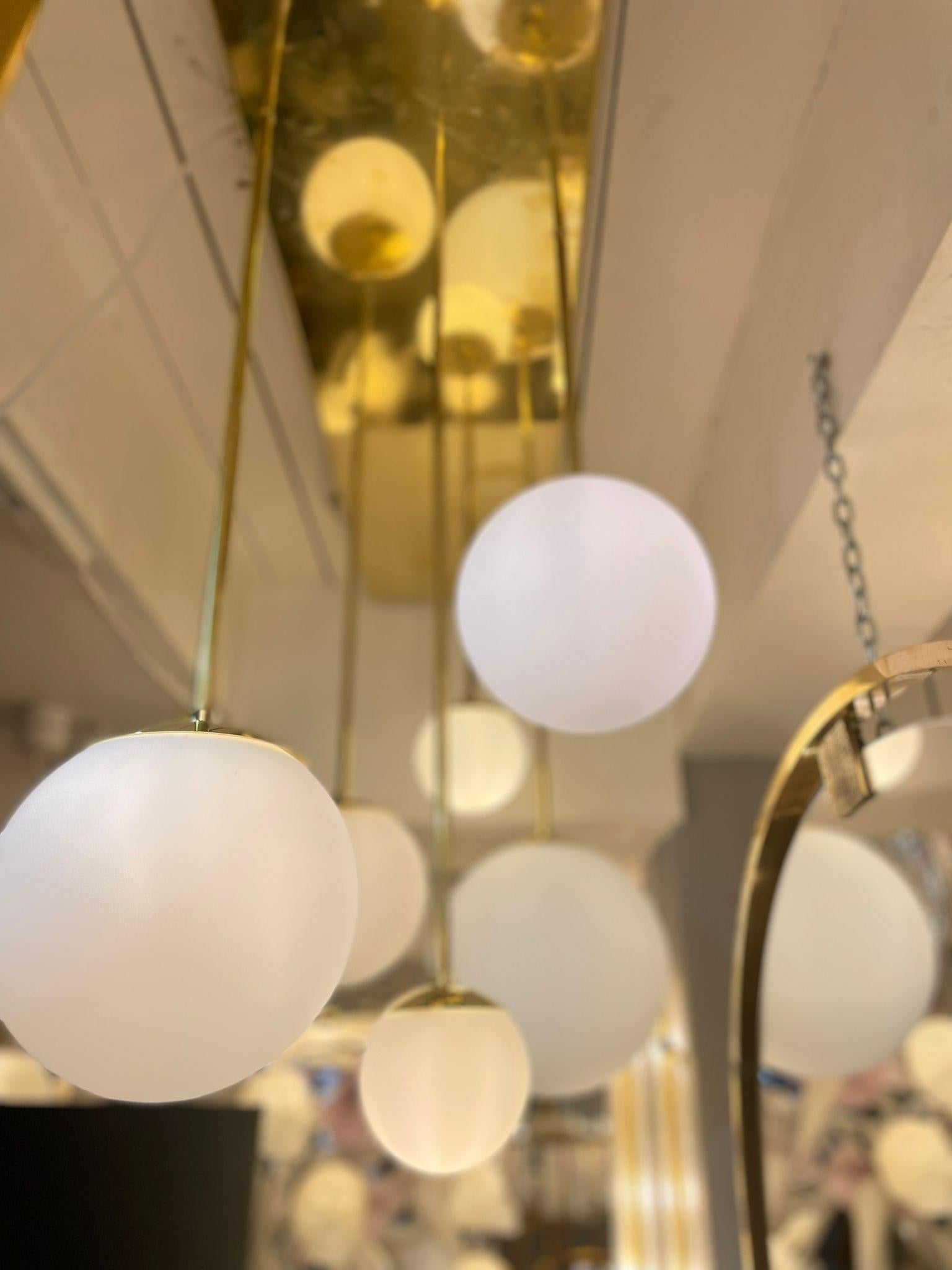 Italian chandelier in brass with 6 spheres in frosted glass. Spheres are in different dimensions and length. Its spherical shape brings roundness and comfort to your interior for more softness and delicacy. In a hallway, an entrance, a living room