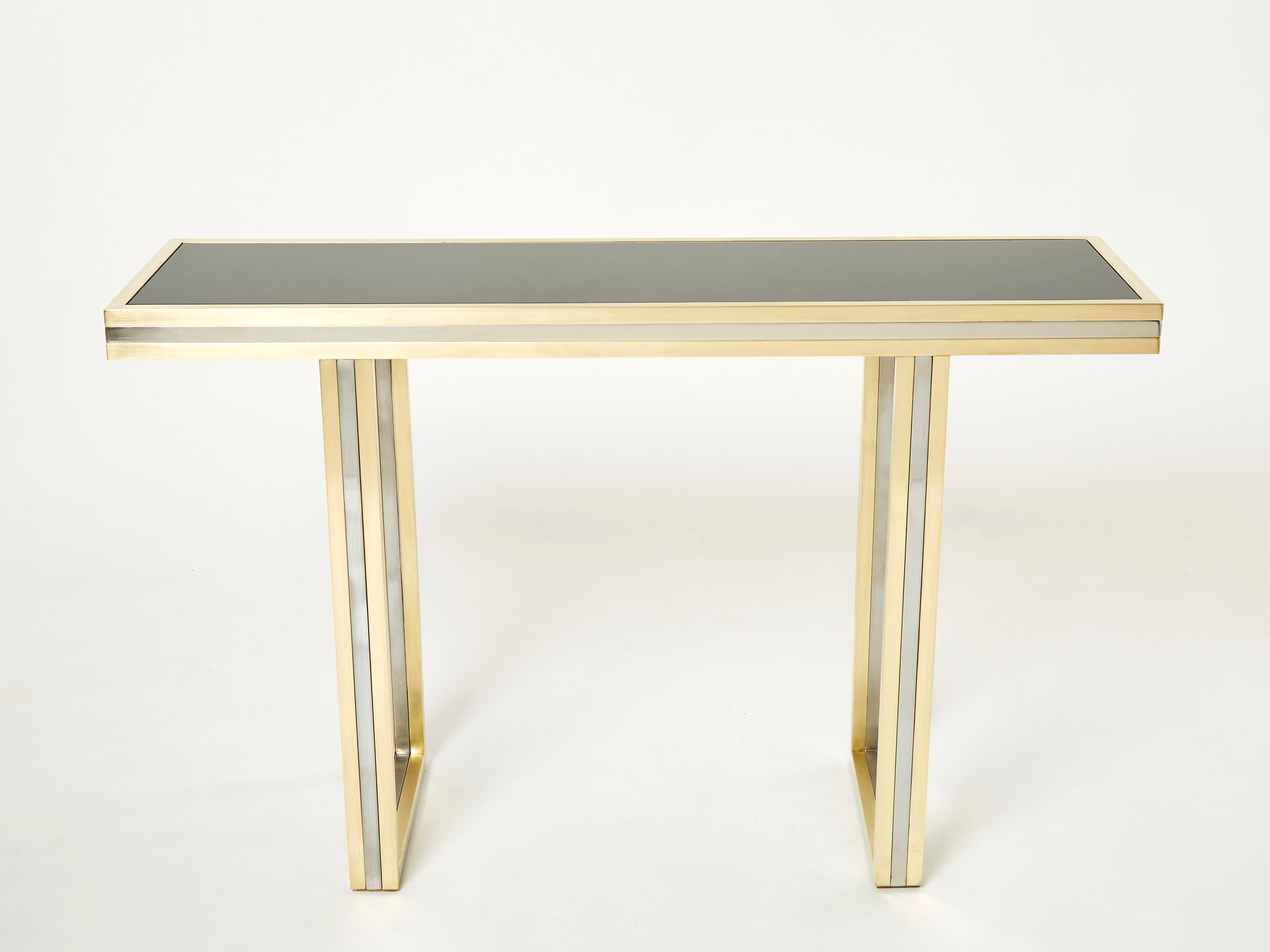 A beautiful piece of design, this console table deserves to be the focal point of your entrance or living room. Symmetrical brass and chrome elements strike through a black opaline glass top, the result being an impressively sleek decorative piece.