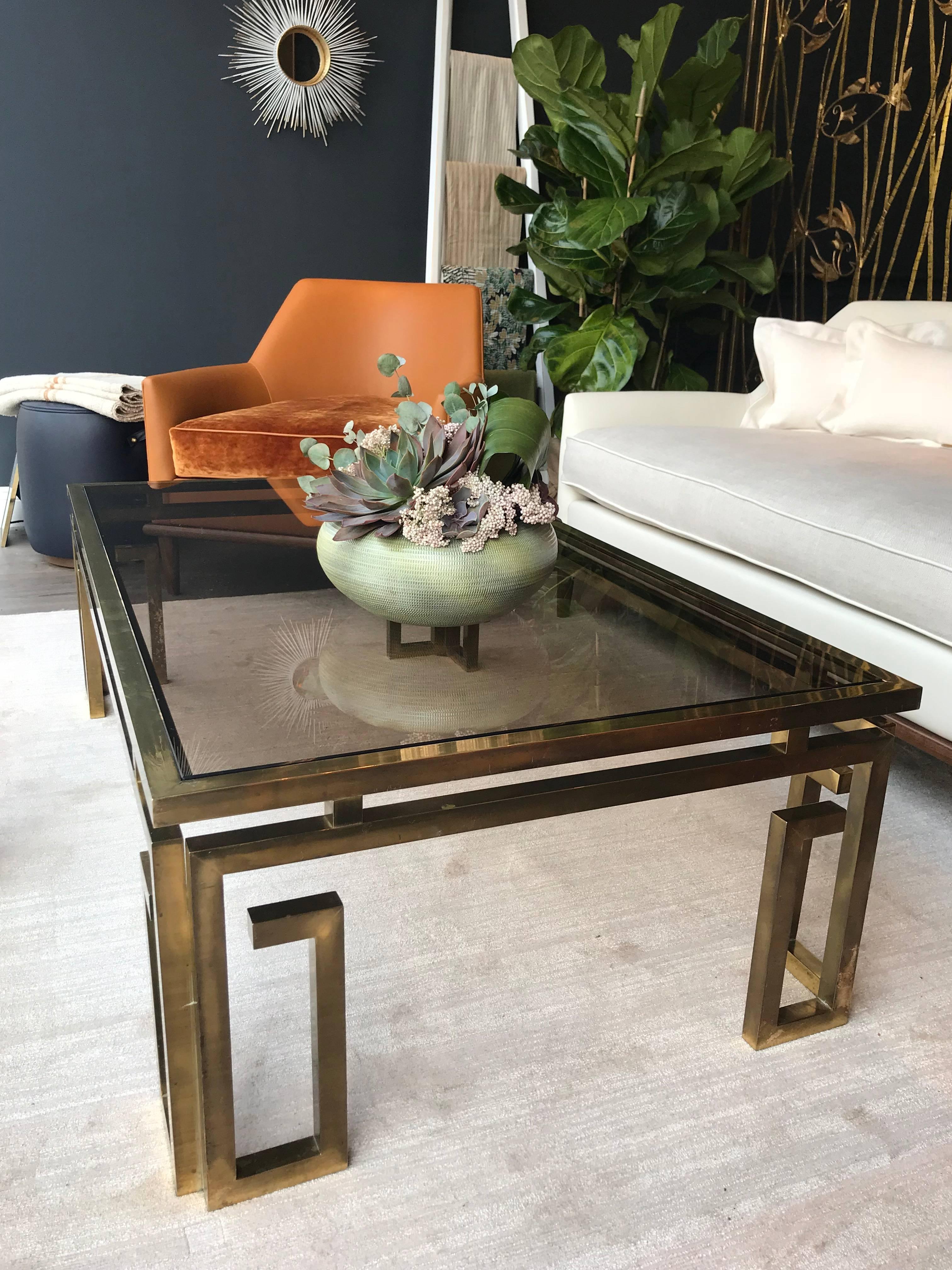 An Italian brass coffee table with ornate Greek key legs and smoked glass top.