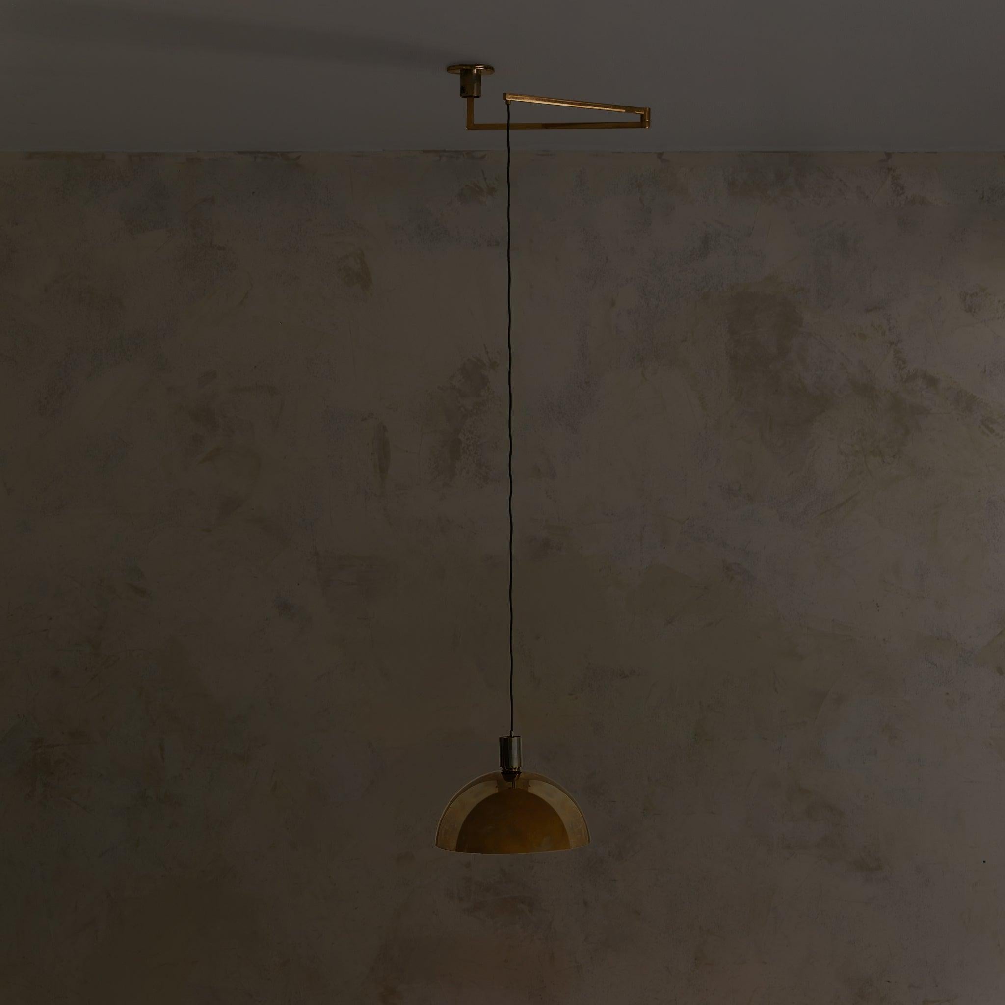 An Italian pendant light attributed to Franco Albini for Sirrah, 1968. The design is anchored by a domed brass shade, suspended from a slim black cord and pivoting brass arm. Over time, the polished surface has developed a moody, atmospheric
