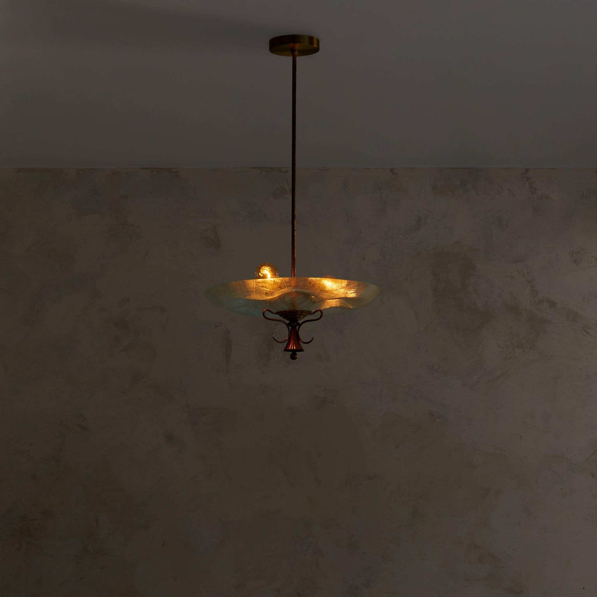 A 1950s Italian pendant light in the manner of Pietro Chiesa for Fontana Arte. The wide, handblown glass dish floats from a single brass rod—its clear surface etched with delicate lines and elliptical impressions that catch and refract the light.