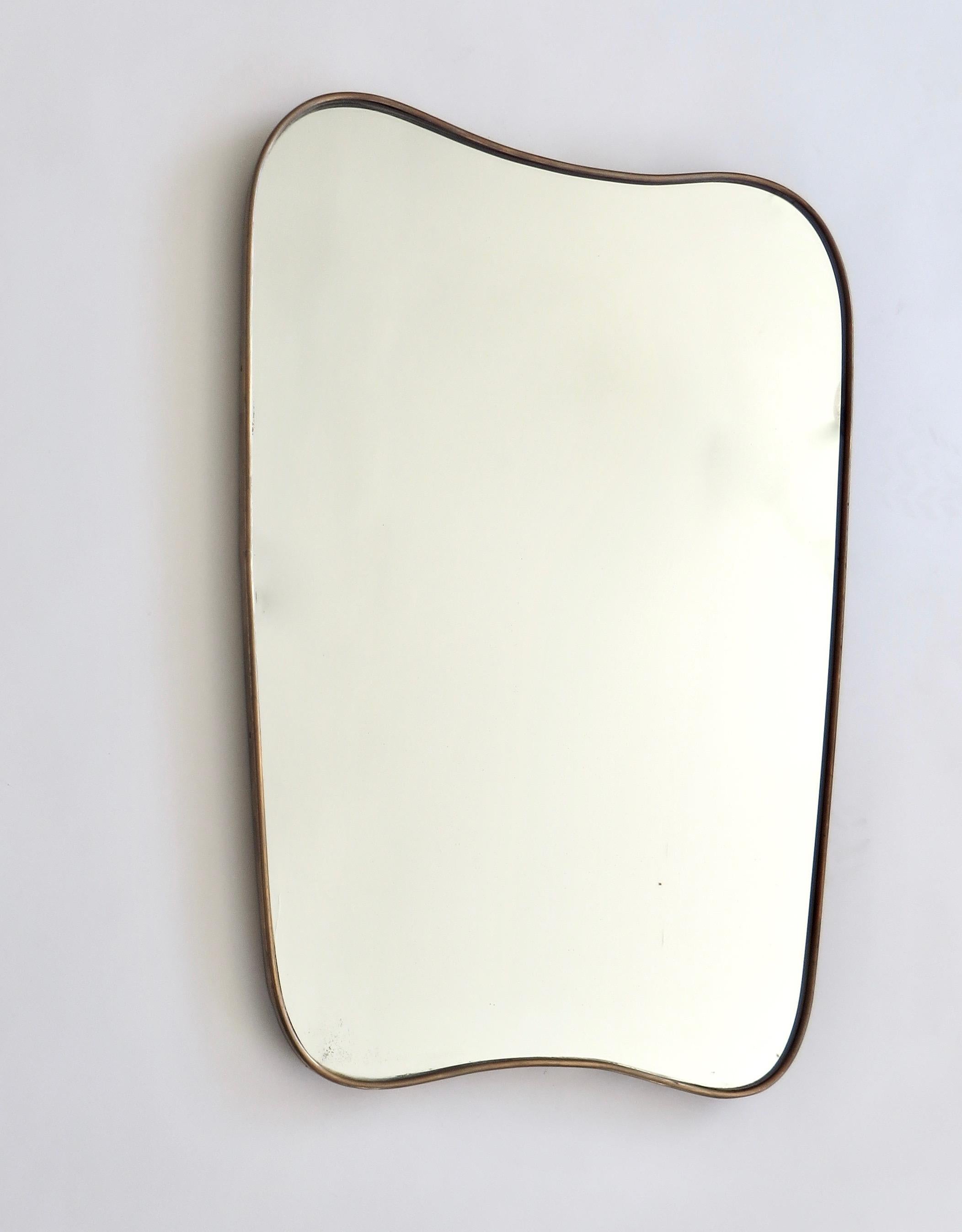A gently rounded sloping shaped Italian brass framed mirror with beautiful patina and no flaws to the original mirror, circa 1950. 
The mirror rounds gracefully at the bottom reflection the curves at the top. 
Nice patina on the brass. 
Small