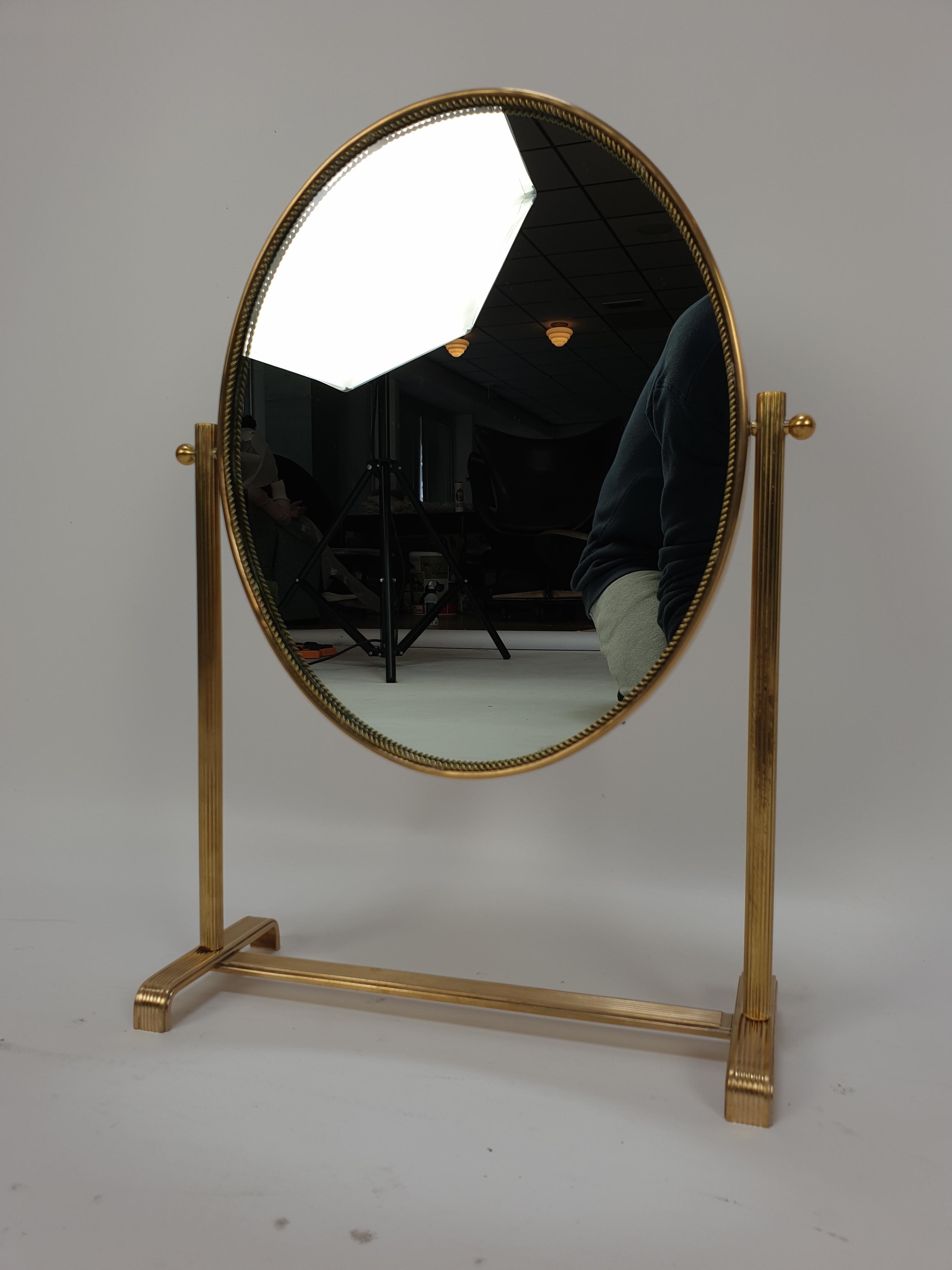 Gorgeous vanity mirror with full brass frame and base. Made in Italy in the 1950s. The round frame has decorative details. The mirror can be turned around. The back plate is made of dark wood. The mirror glass has been renewed, nevertheless there is