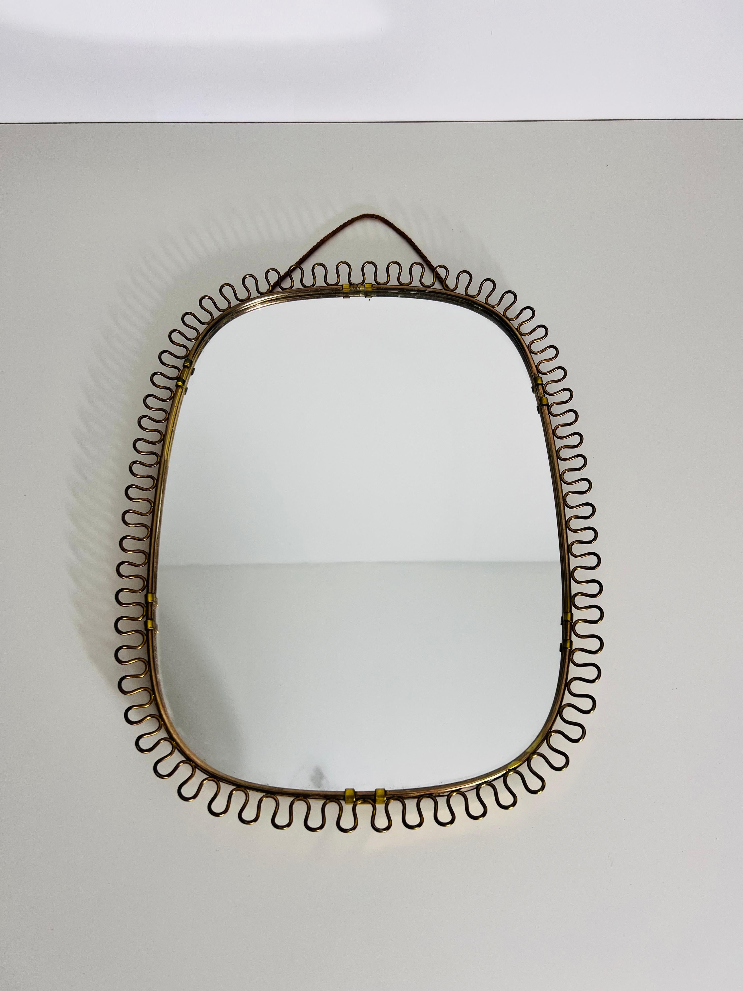 Vintage Italian wall mirror from the 1960s, crafted entirely from brass. The mirror is surrounded by an elegant brass frame featuring a distinctive comb-like ornamentation around the edges. This extraordinary design creates a unique and eye-catching