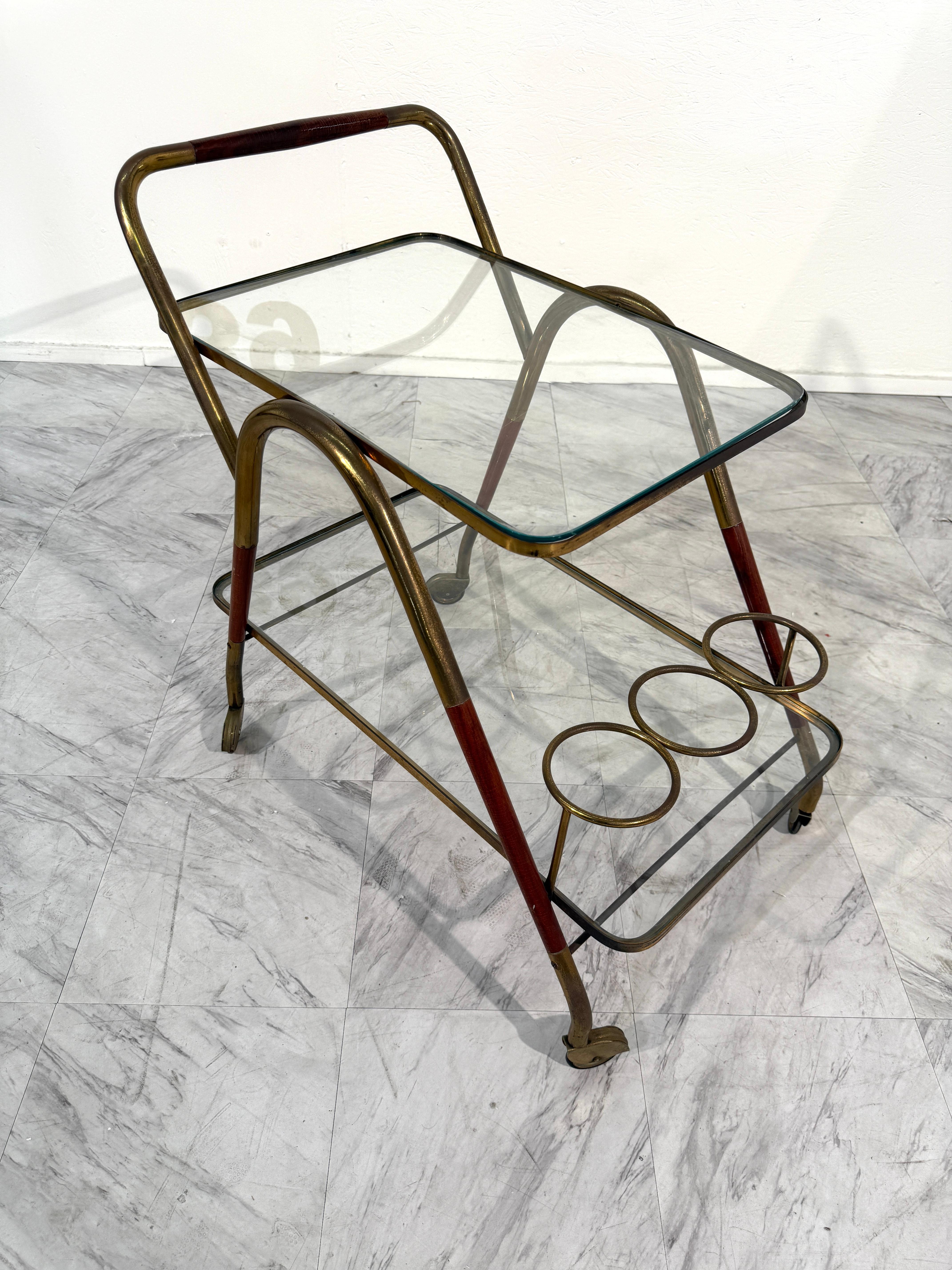 Elegante carrito de bar italiano de mediados de siglo, con una escultural estructura de latón de líneas curvas y detalles lacados en rojo. El diseño de dos niveles incluye estantes de cristal transparente, que ofrecen un amplio espacio para servir