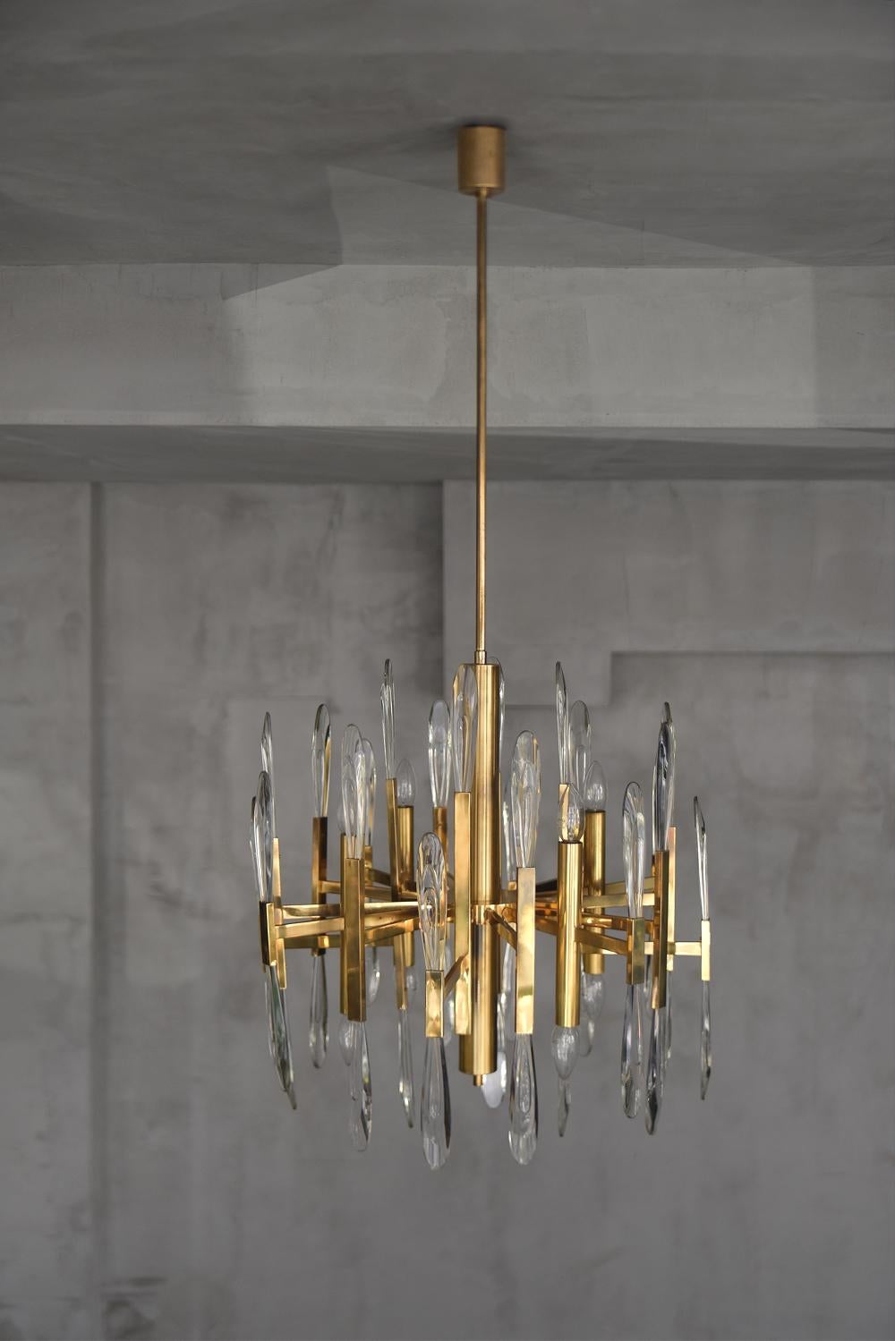 This stunning Midcentury Modern chandelier by Gaetano Sciolari was manufactured in Italy during the 1970s. It is made from highly polished brass, has a beautiful glass drops in the holders and is a work of art. This form showcases a blending