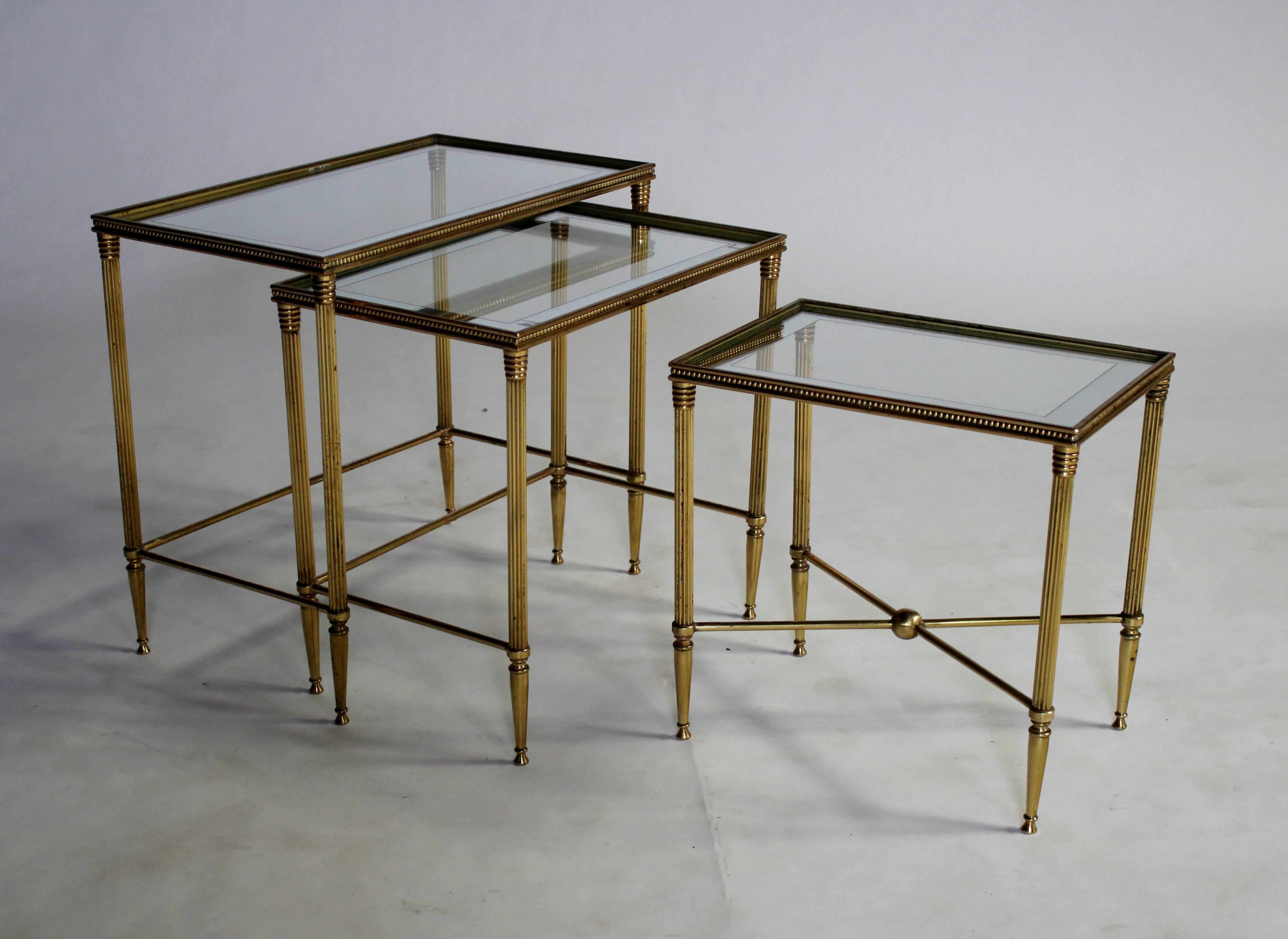 Set of three Hollywood Regency nesting tables in brass with a natural aged patina and original mirror-framed glass tops. Labelled, 