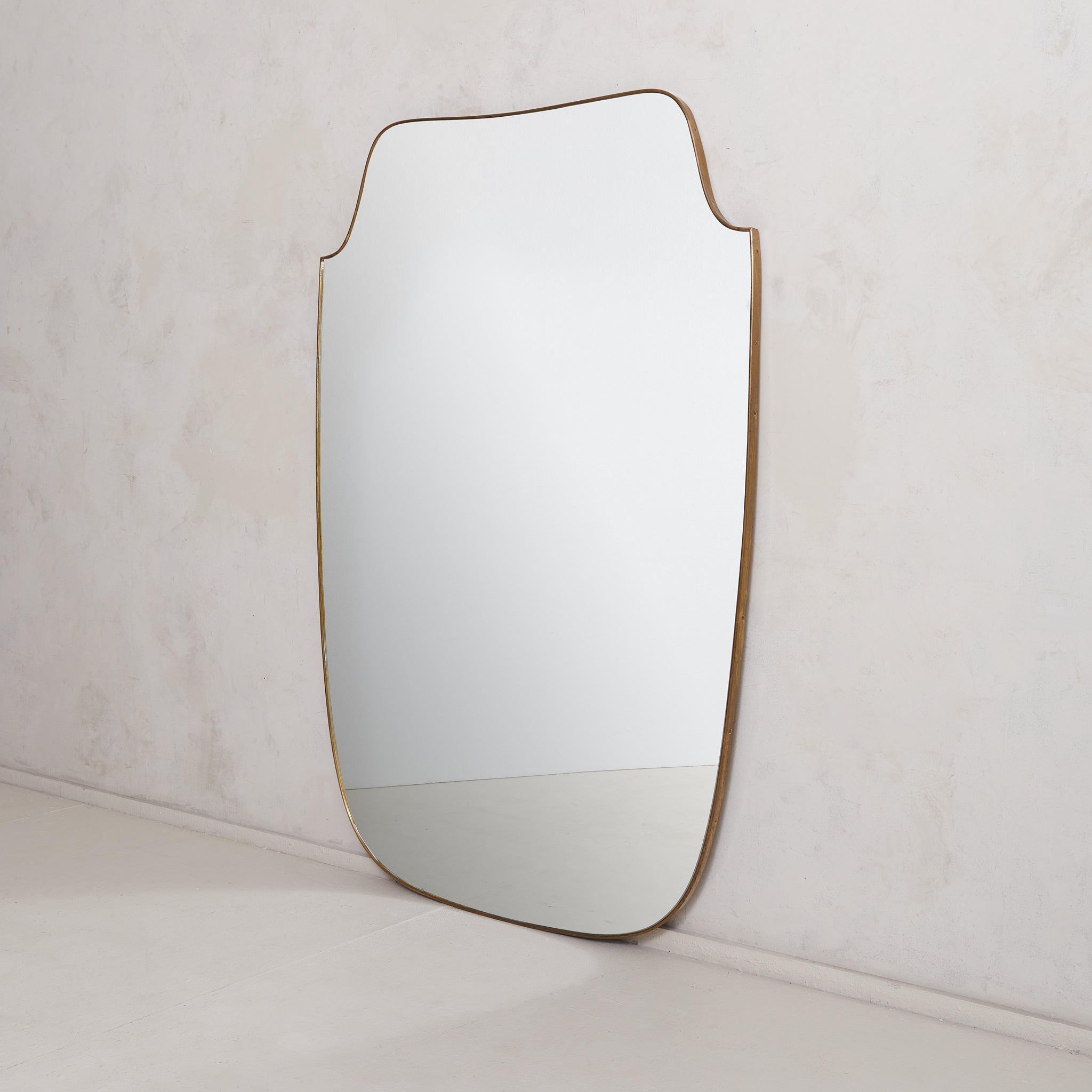 Vendus et tarifés individuellement.

Miroir mural encoché italien des années 1970 présentant d'élégantes courbes le long de la partie supérieure et une silhouette subtilement effilée. Ce miroir a un cadre délicat en laiton avec une belle patine