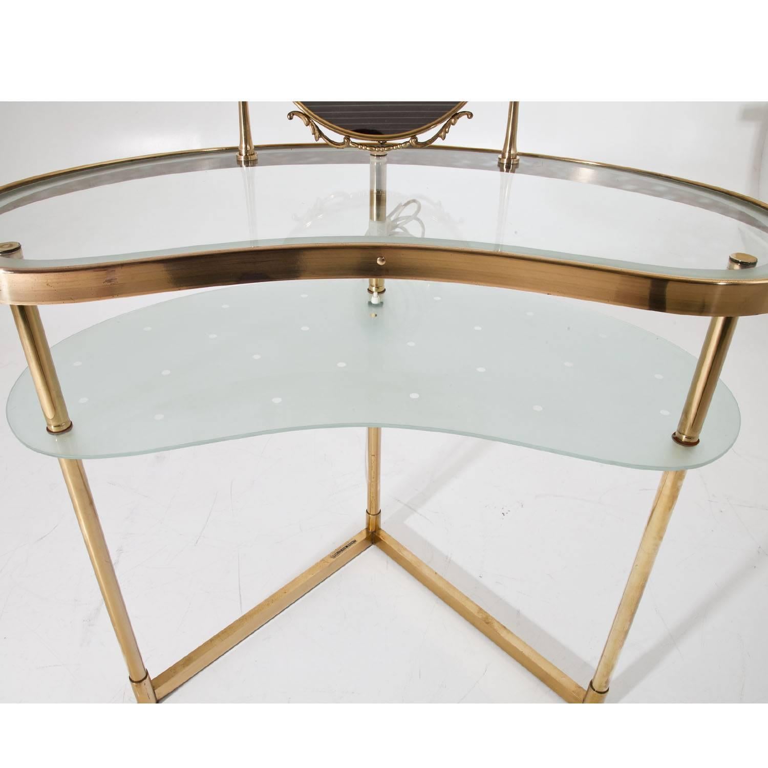 Midcentury vanity table on a three-legged brass base with a kidney-shaped tabletop and one shelf, decorated with dots. The oval mirror is tilt able. The vanity can be illuminated from below with one light bulb, creating the perfect lighting
