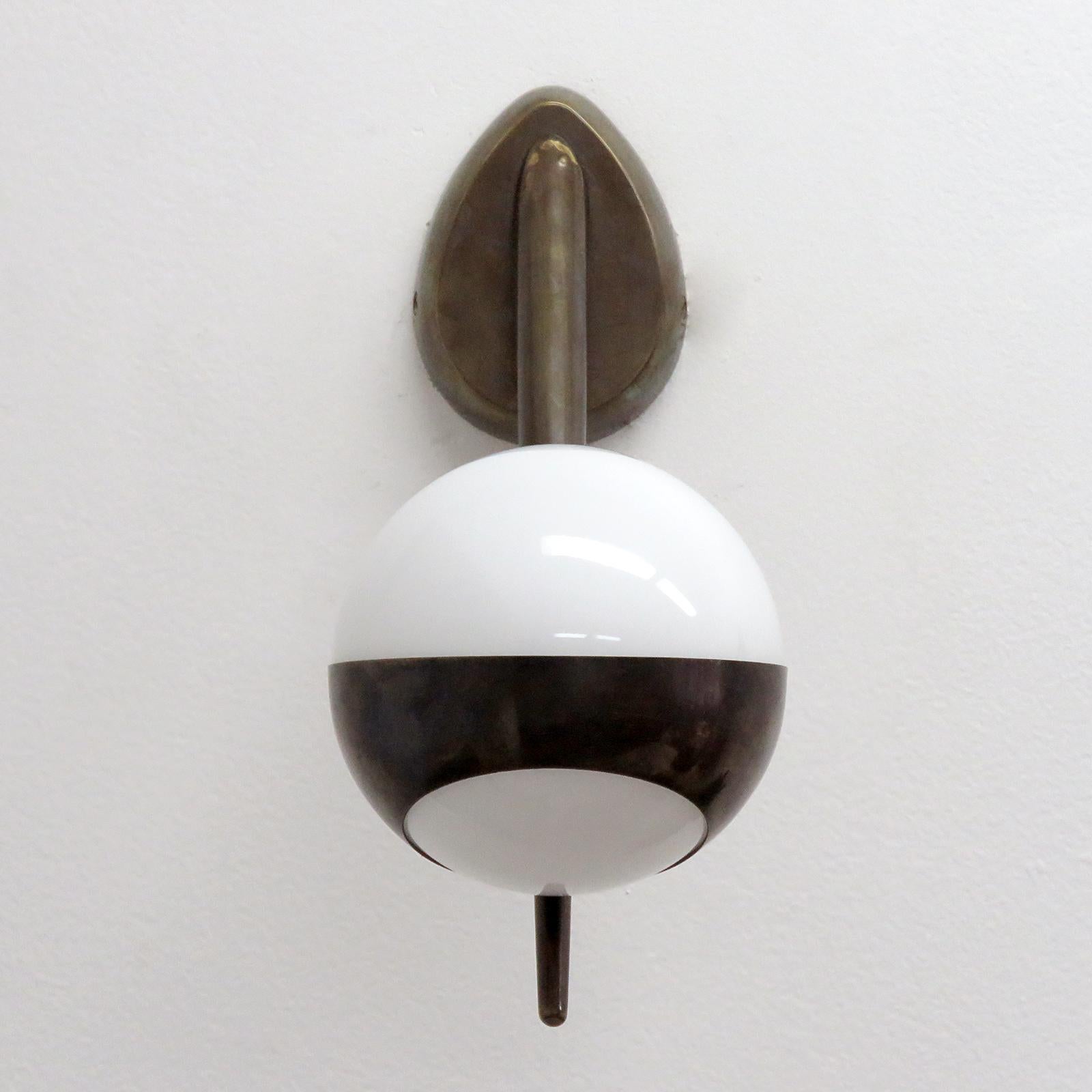 Wonderful Italian patinated brass sconces, with a white cased glass globe on a cantilevered arm, one G9 socket, max. wattage 75w each or LED equivalent, wired for US standards or European standards (110v/220v), UL listing available upon request for