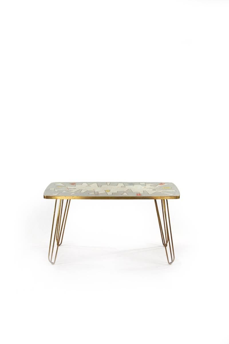 Berthold Müller side table with glass mosaic, Italy, 1950s. The Mosaic is designed with geometric forms in white, grey, blue and yellow. The Table legs are made of brass and form a loop-shaped leg.


  