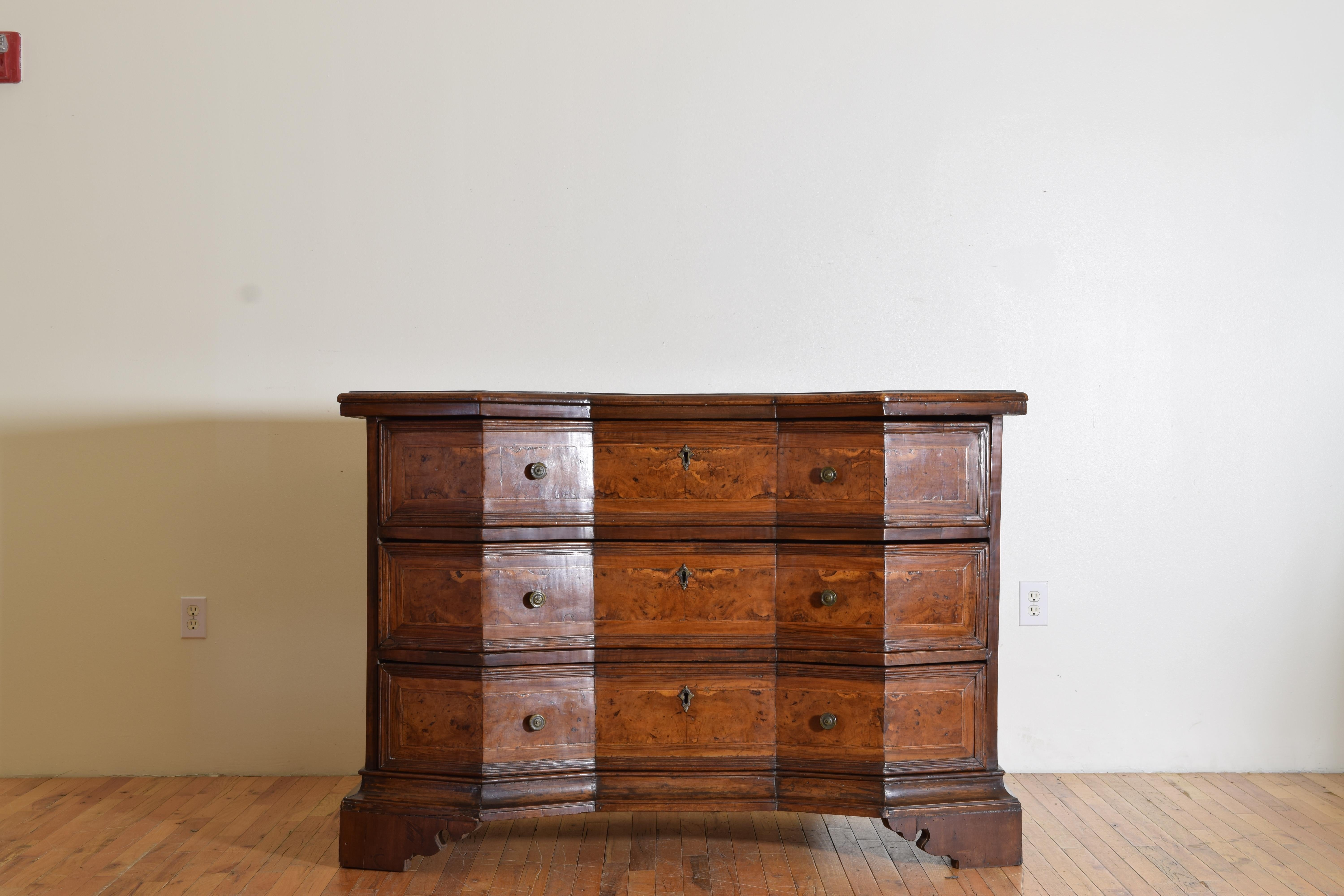 Having a shaped top with canted corners and a recessed center and a molded edge, the drawer fronts all covered in burl walnut veneer and retaining antique hardware, raised on bracket feet