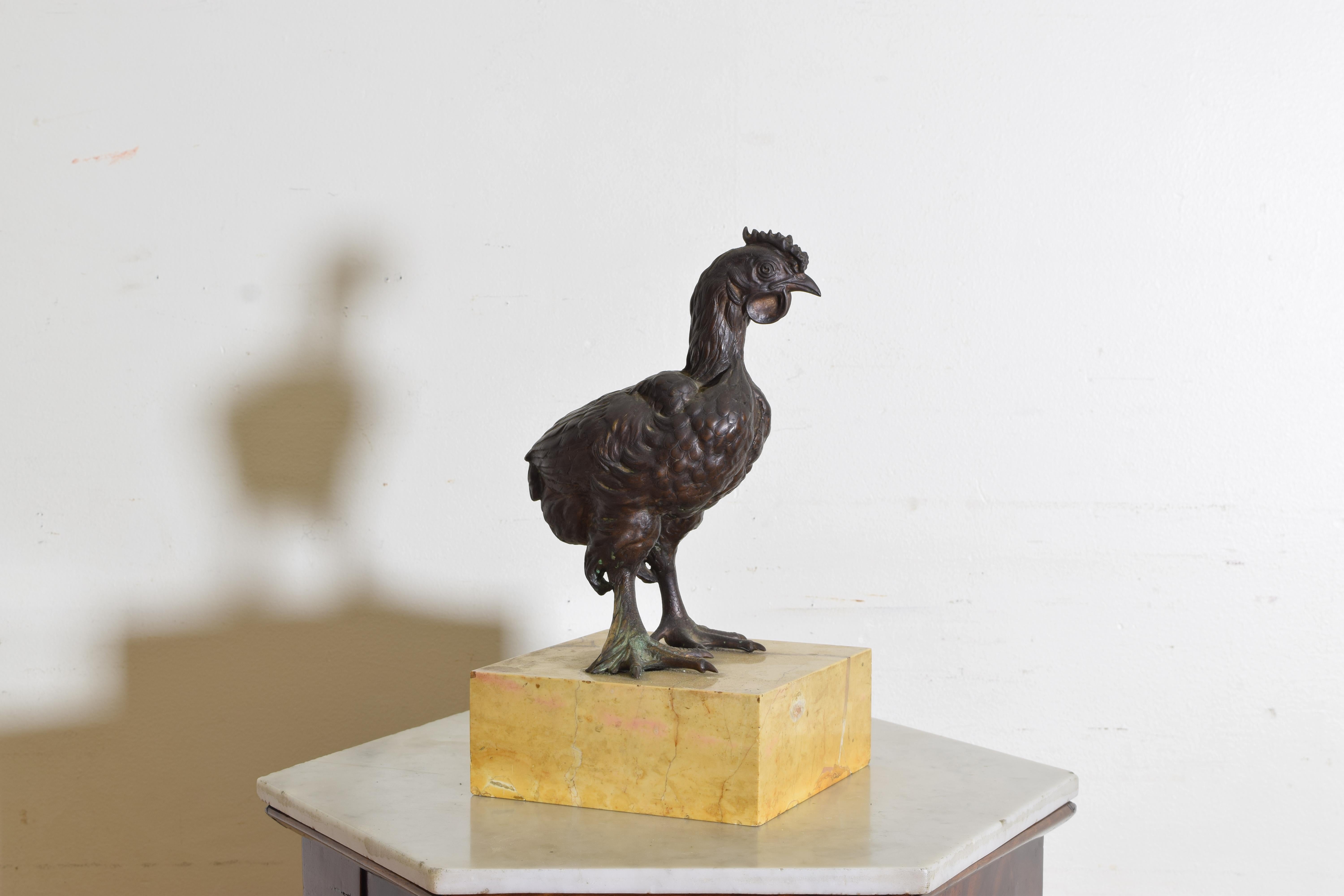 The upright young rooster gazing slightly to its left, its webbed feet mounted firmly atop a rectangular solid marble base.