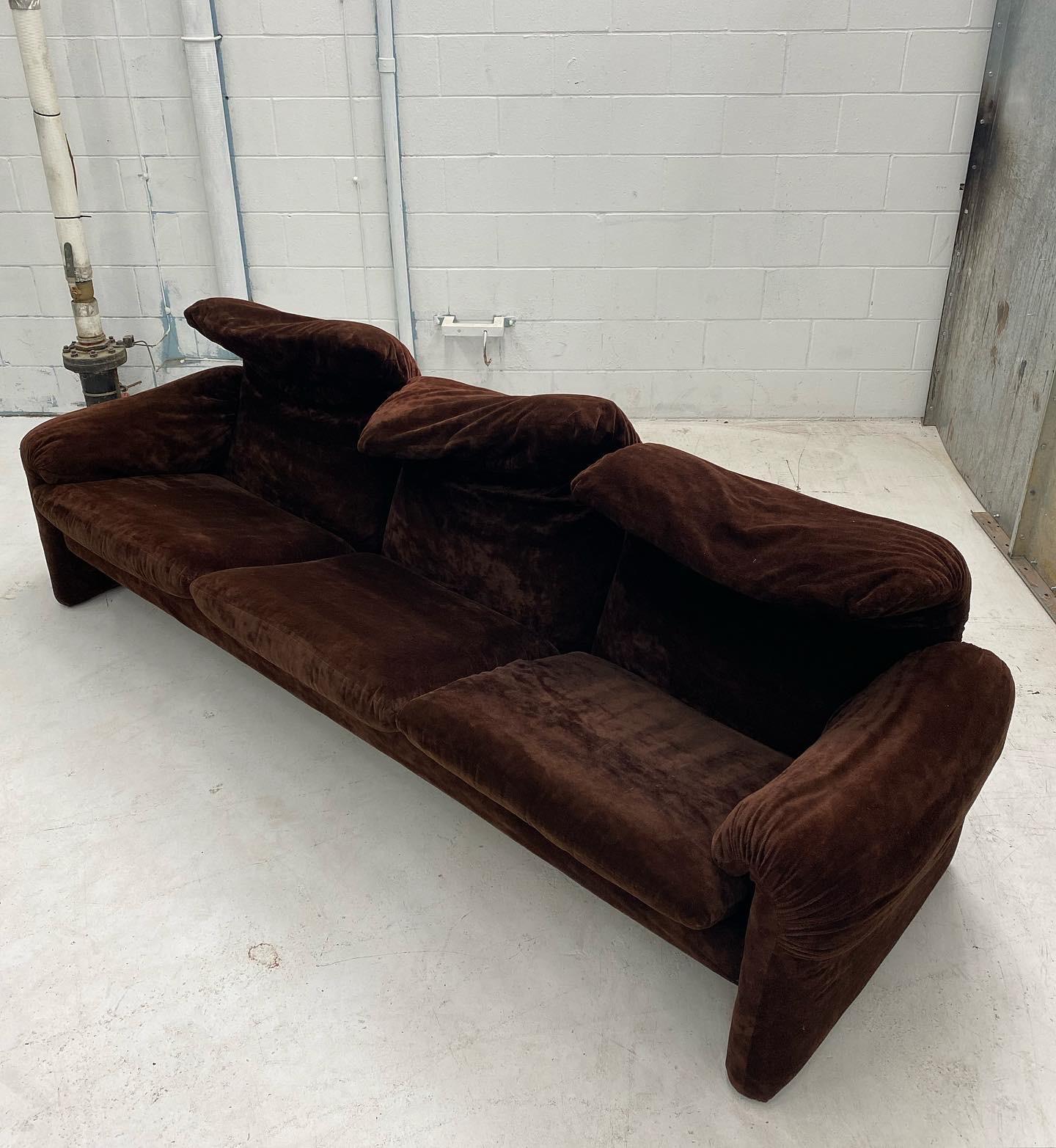 Maralunga three-seater sofa covered entirely in dark brown velvet. It has a steel structure consisting of two large lateral legs from which the armrests start, the back and the base of the seat. The seat is made up of 3 rectangular cushions. The