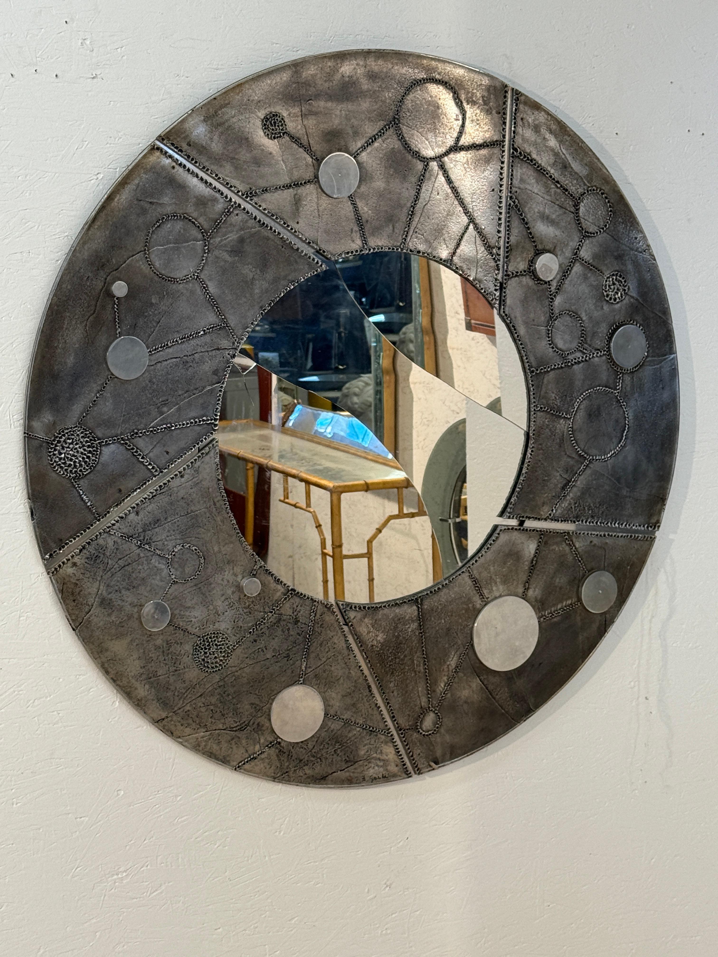 A striking Italian round wall mirror encircled by a wide sculptural metal frame with Brutalist-inspired detailing. The surface features abstract circular motifs and textured patterns, giving it a bold, industrial aesthetic. Both functional and