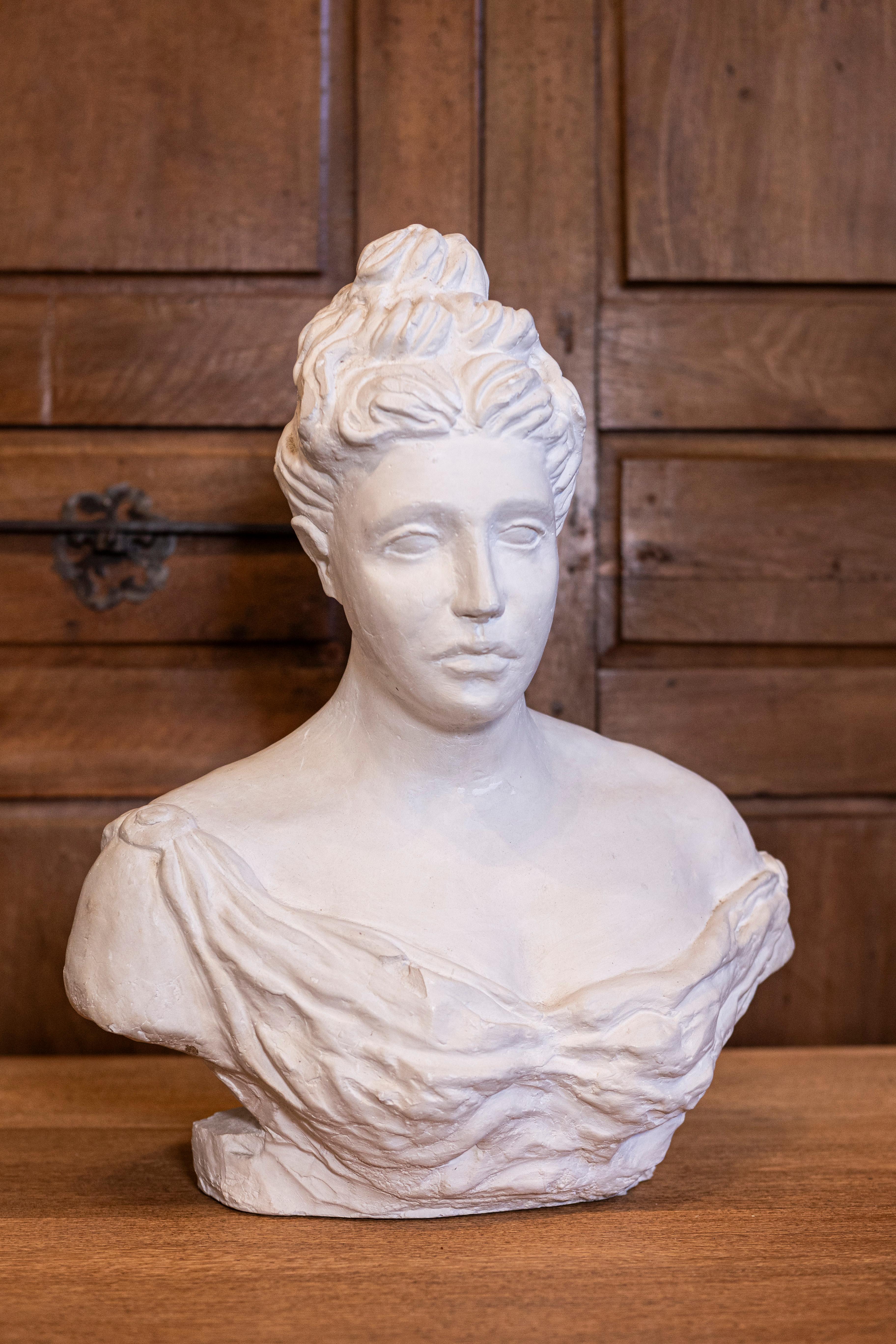 An Italian bust of a woman wearing a sleeveless and creased dress attached with a fibula. This elegant 20th-century Italian bust captures the timeless beauty and grace of a woman adorned in a sleeveless, creased dress, secured on one side by a