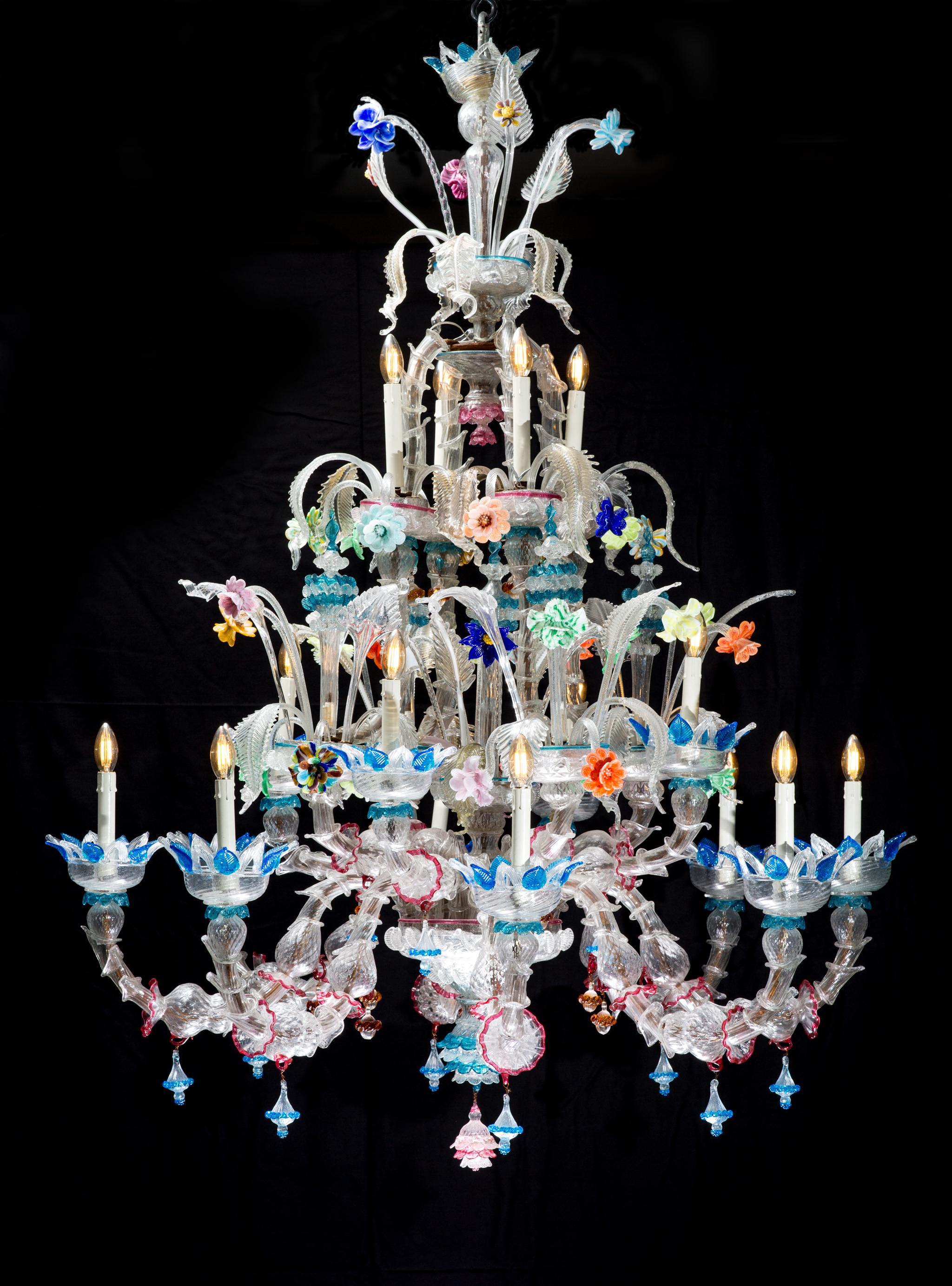 A very big colored Murano chandelier from Venetia in Italy. The chandelier was made in the mid-century period.
The chandelier has a total of 16 arms. 12 of the 16 arms have a light bulb and the remaining 4 arms have an ornated peak.
At the top of