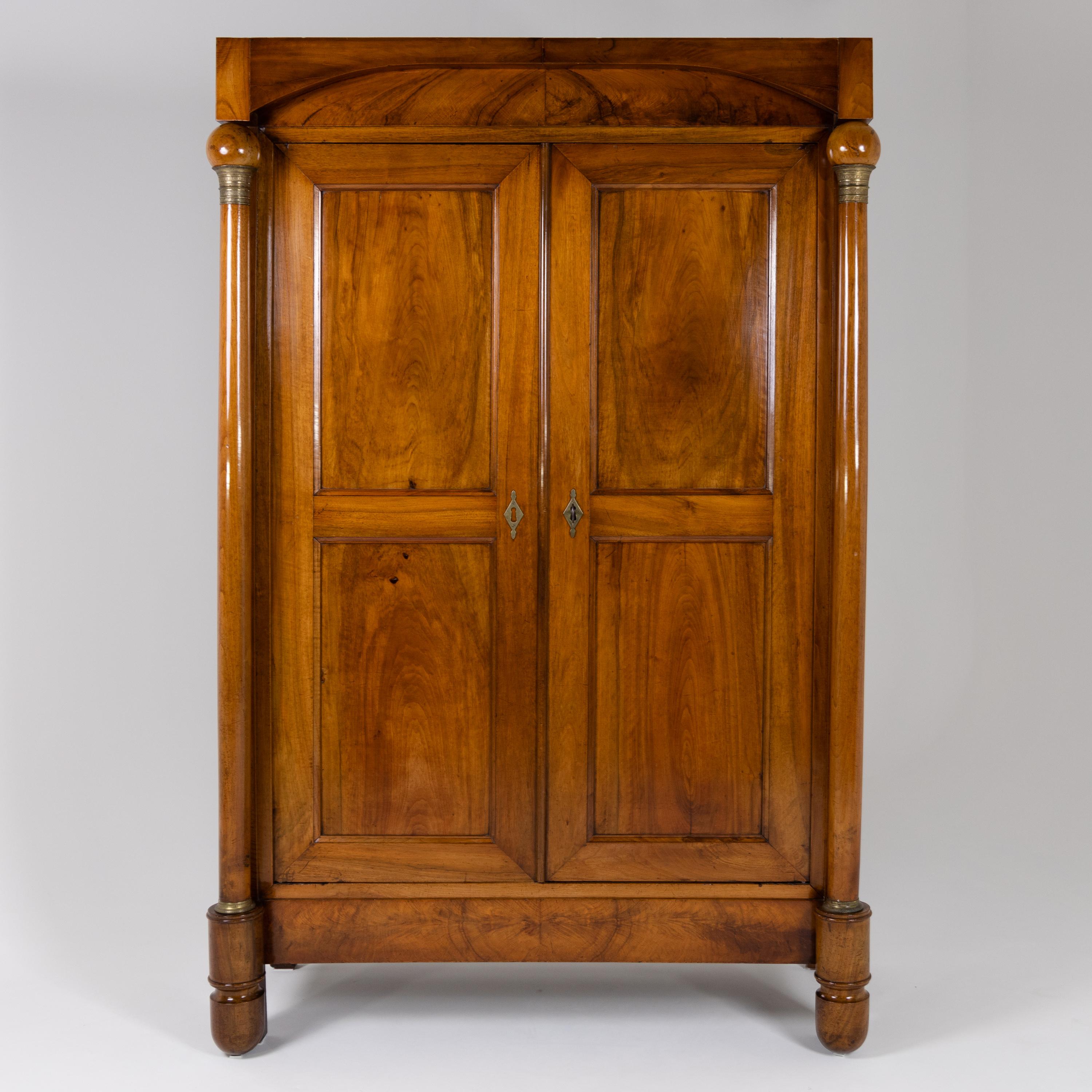 Two-door Italian cabinet with coffered doors and sides and column supports on conical profiled legs with brass capitals and bases. The columns carry sphere finials which support the segmentally cut straight cornice. Solid Mahogany and veneered. The