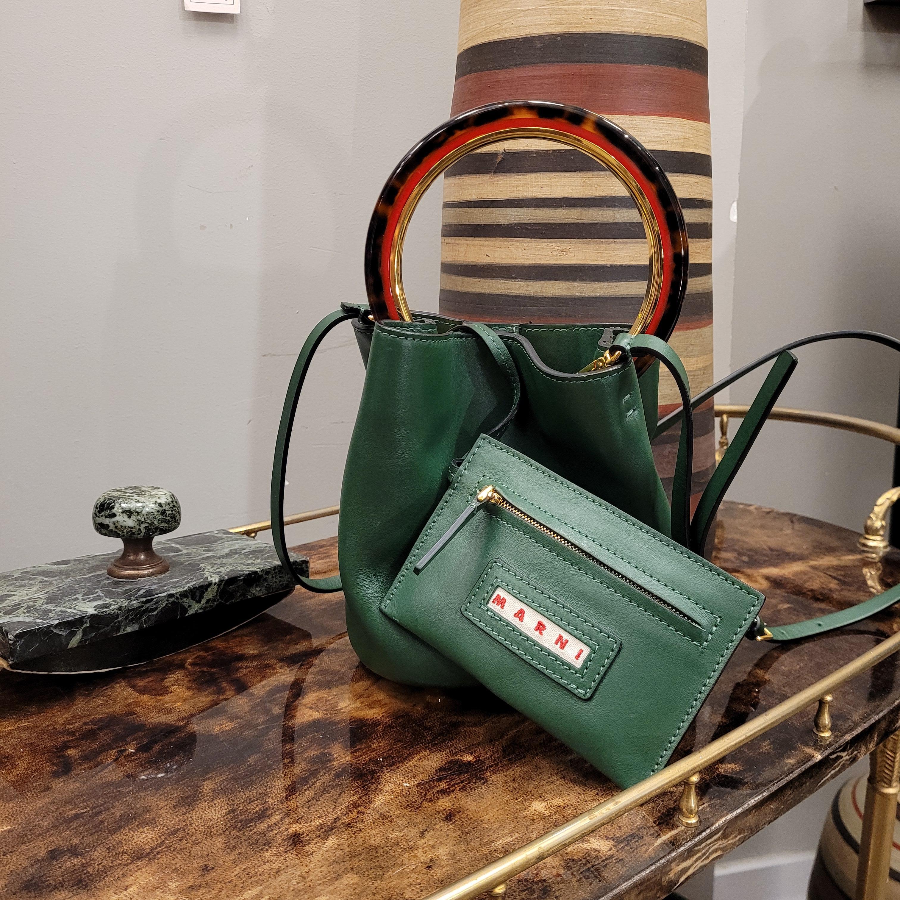 Beautiful calfskin bucket bag in a lovely English green colour.
Leather shoulder strap with gold metal hooks.
Circular handle in tortoiseshell imitation for hand holding. Wallet/purse independent and attached to the bag through a leather strap,