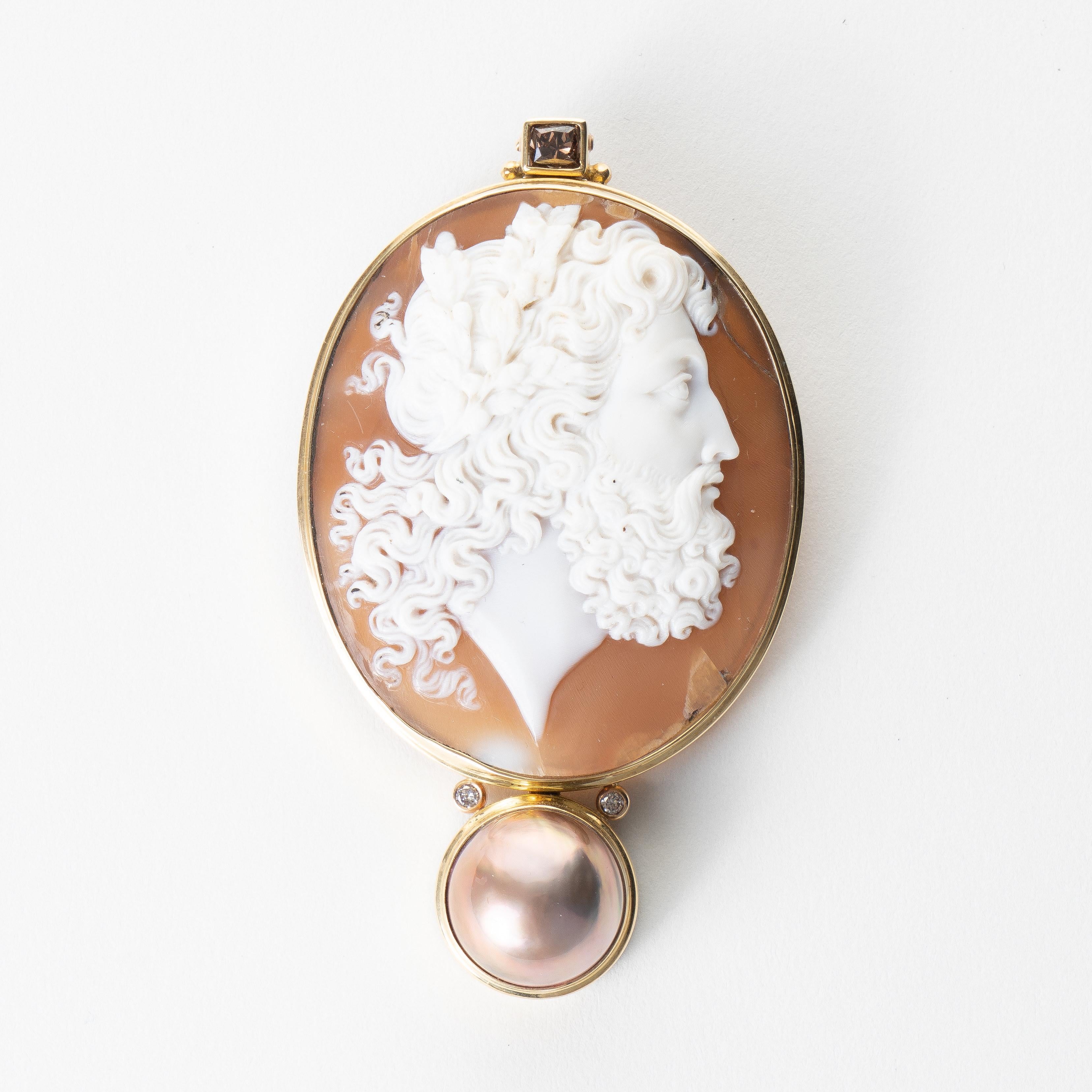Exquisitely carved Italian oval shell cameo profile pendant of Zeus remounted in a custom 18K gold bezel with enhancements of a single mabé pearl flanked by a pair of white diamonds, and a square cut cognac diamond mounted above the cameo. 

The