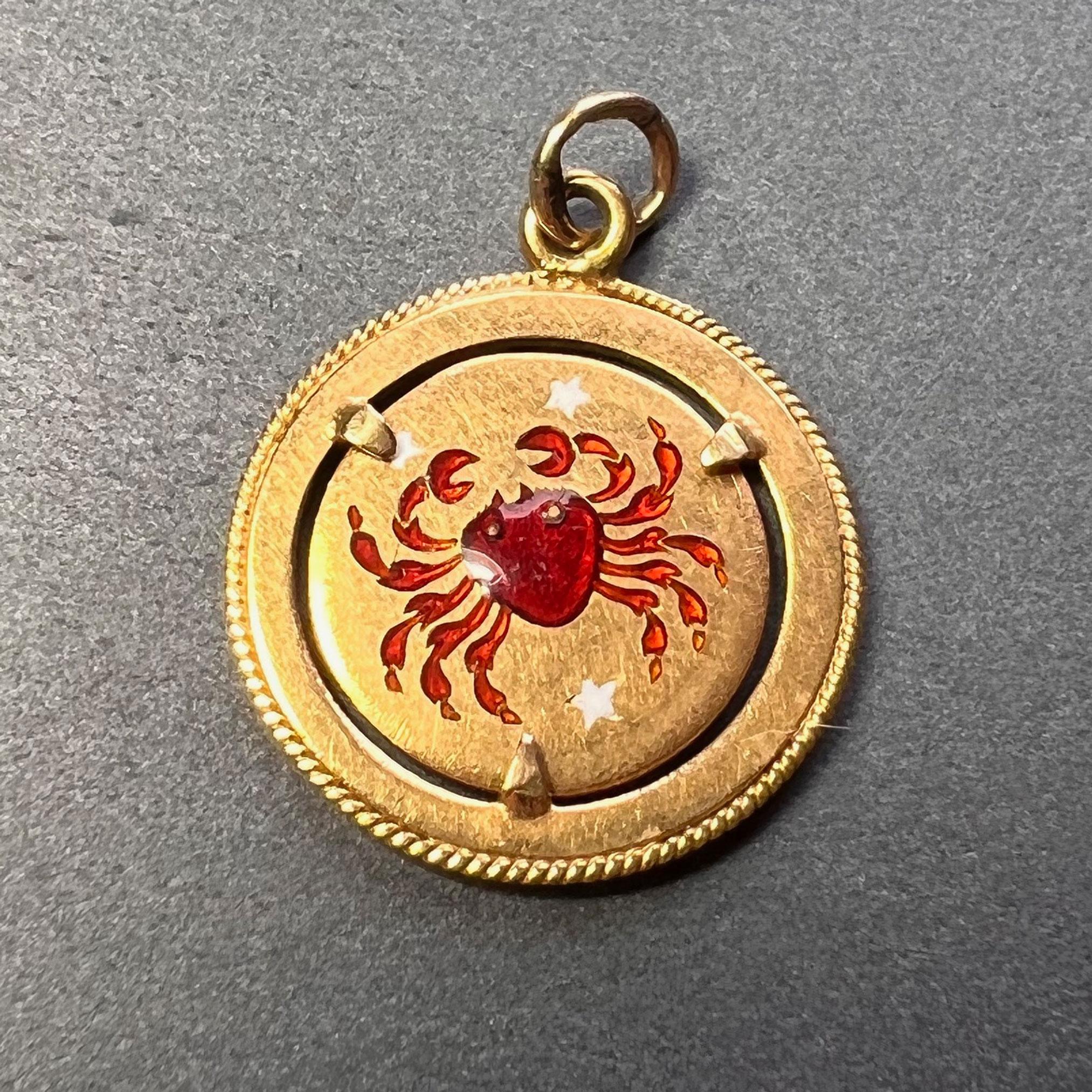 An 18 karat (18K) yellow gold charm pendant designed as a gold disc with enamel crab representing the zodiac starsign of Cancer with three white enamel stars within a gold frame mount with twisted wire edge detail. Stamped 750 for 18 karat gold and