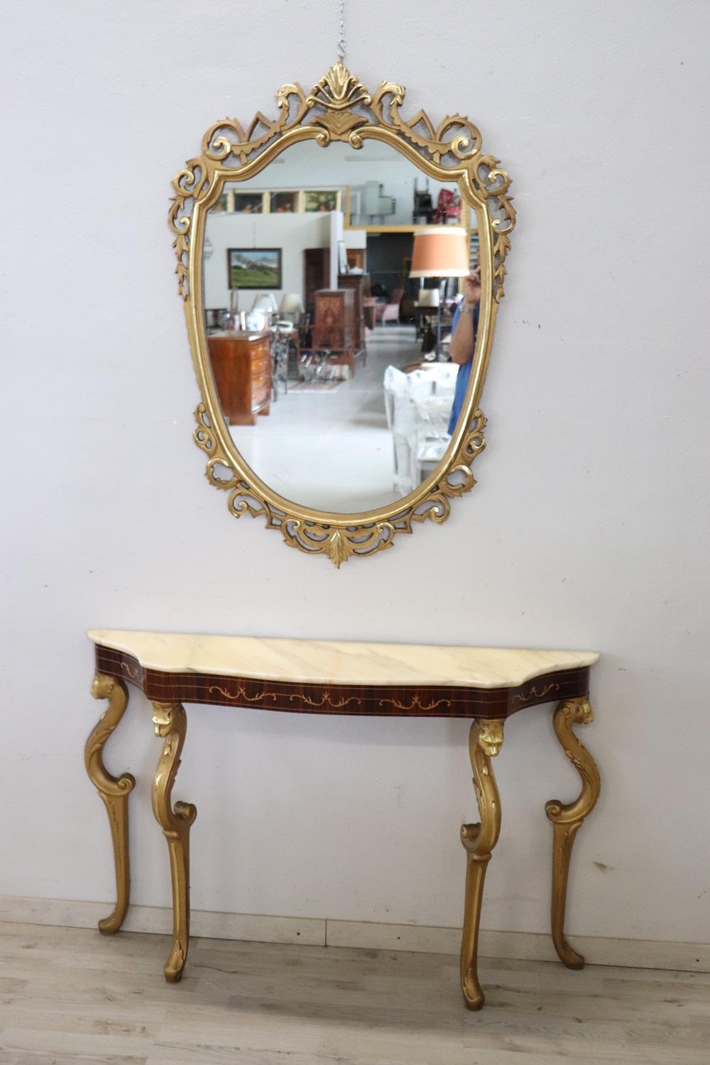 this Italian console made around 1960s is truly refined. Characterized by an eclectic style that combines different decorative elements. The carved wood with gilded elements, the top is in light marble towards the pink. Accompanied by a large mirror