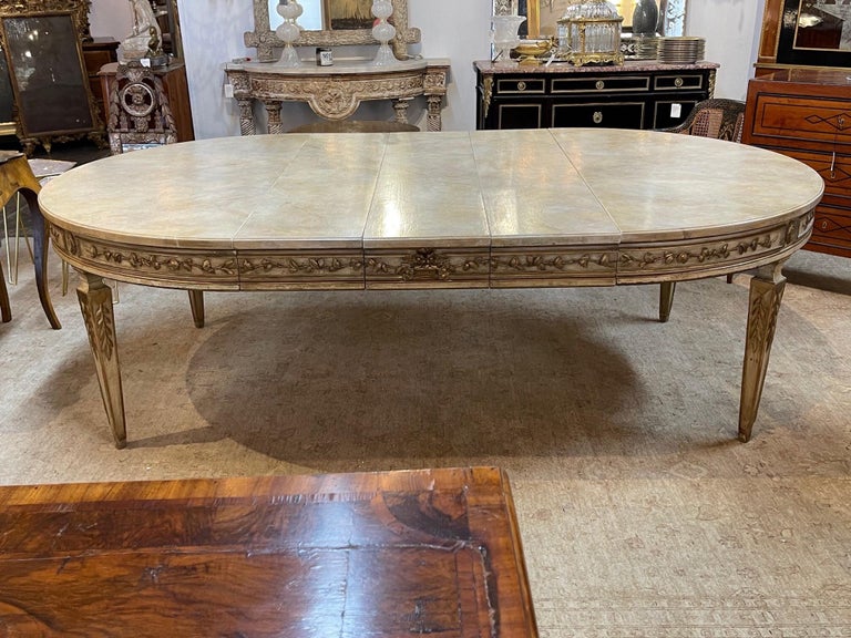 Elegant oval Italian carved and parcel gilt neoclassical style dining table. Featuring lovely carvings and a faux marble painted top. The table is shown with 3 leaves. Makes an elegant statement!