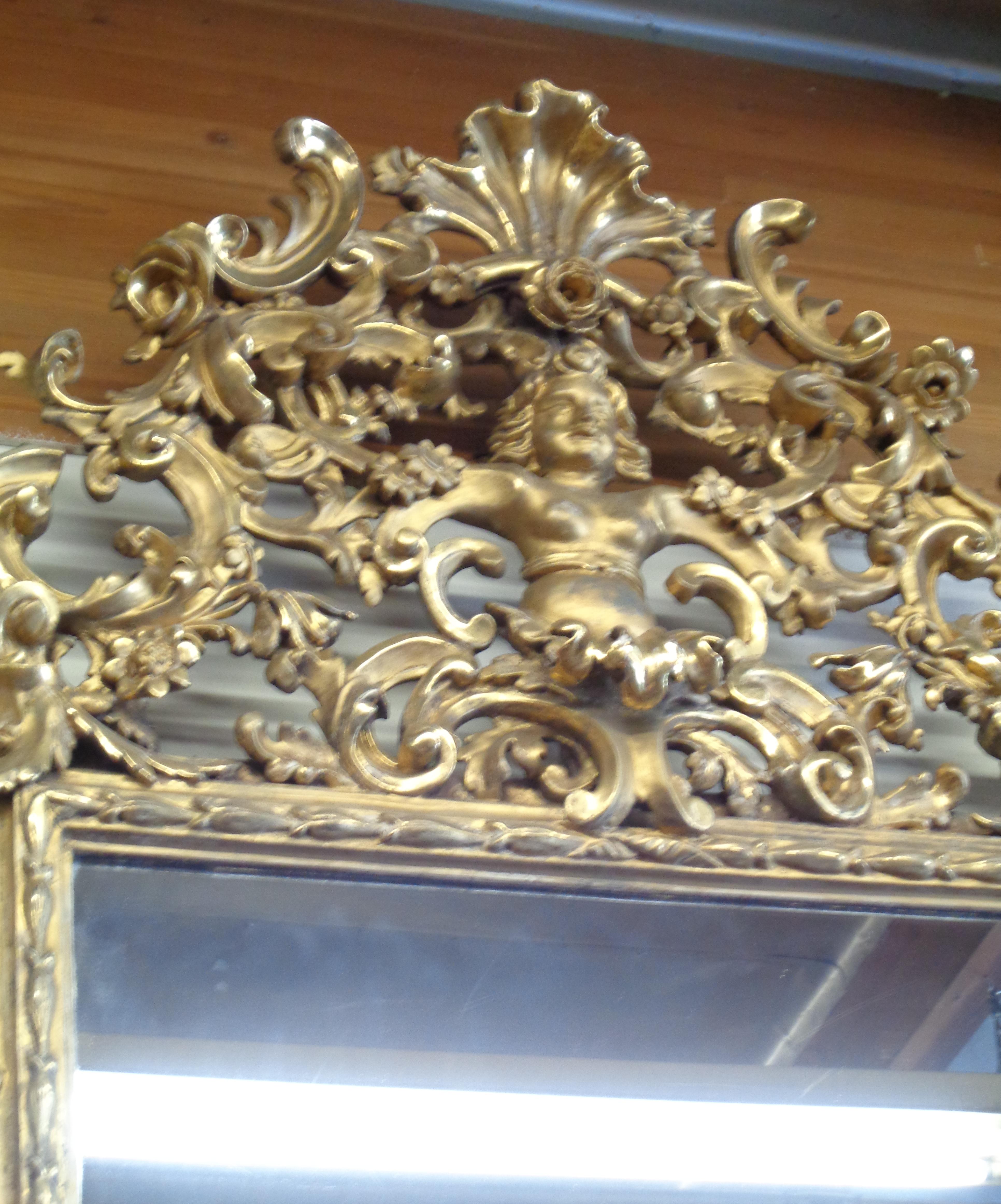 Palatial Italian three dimensionally carved and water gilt mirror. The mirror is magnificently carved throughout. The top of the mirror has a richly carved cornice with a coquille at the top below which is a stylized sea dolphin with a female head.