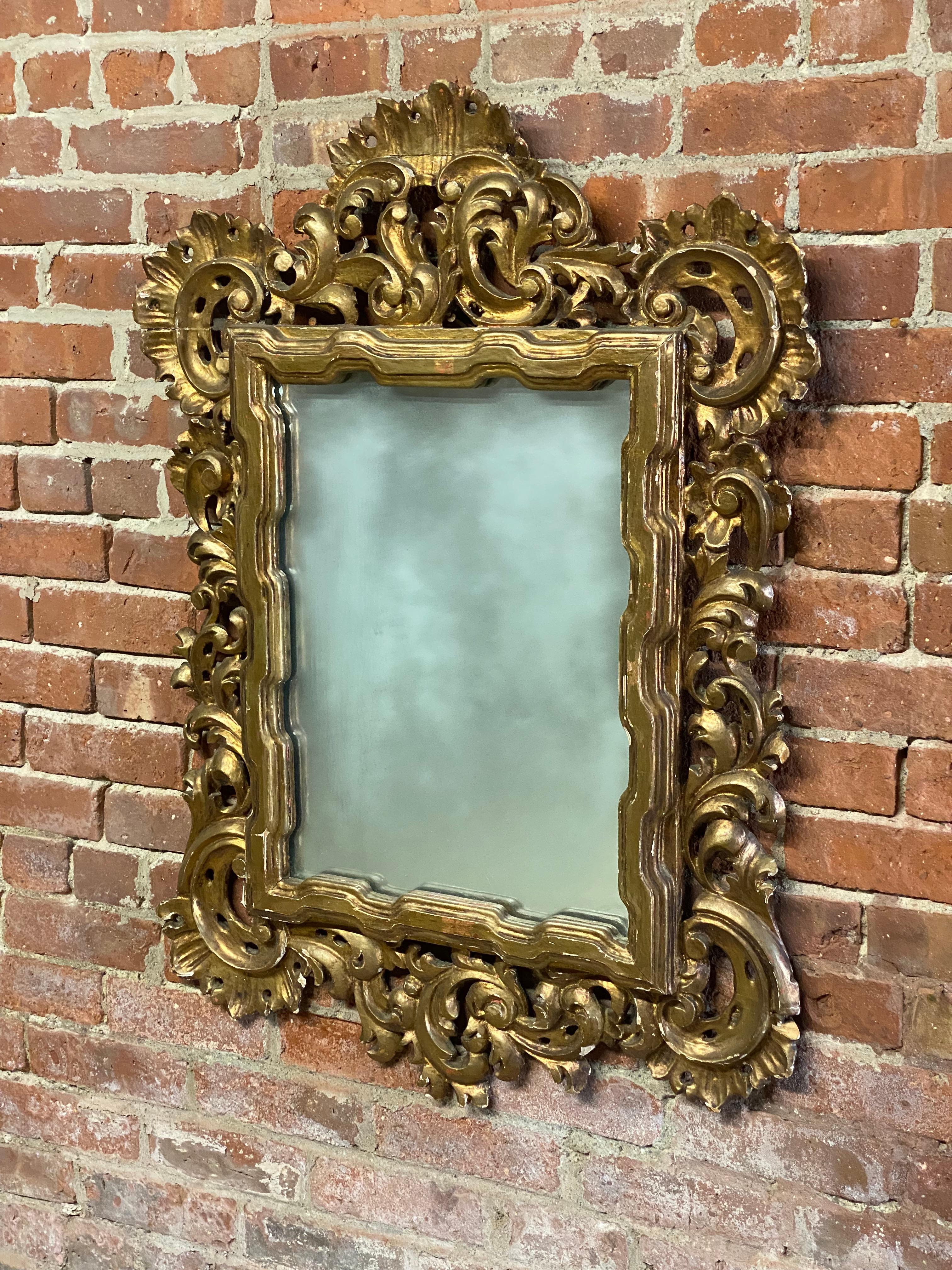 Italian Baroque style carved wood and gilded wall mirror. Sumptuously carved leaf and scrolled motif. The gilded wood shows hints of the typically Italian red bole and gesso under layers. Bole is the 