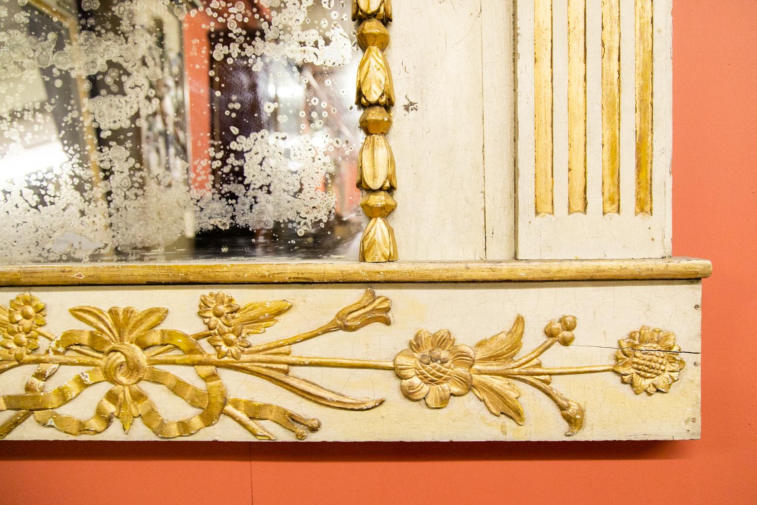Italian carved gilt mirror that is distressed due to age. It depicts angel figures with wings and gold rays in the arch, with dentil molded cornice, stop fluted gilt, painted pilasters, and an arched mirror surrounded by carved high relief flowers.