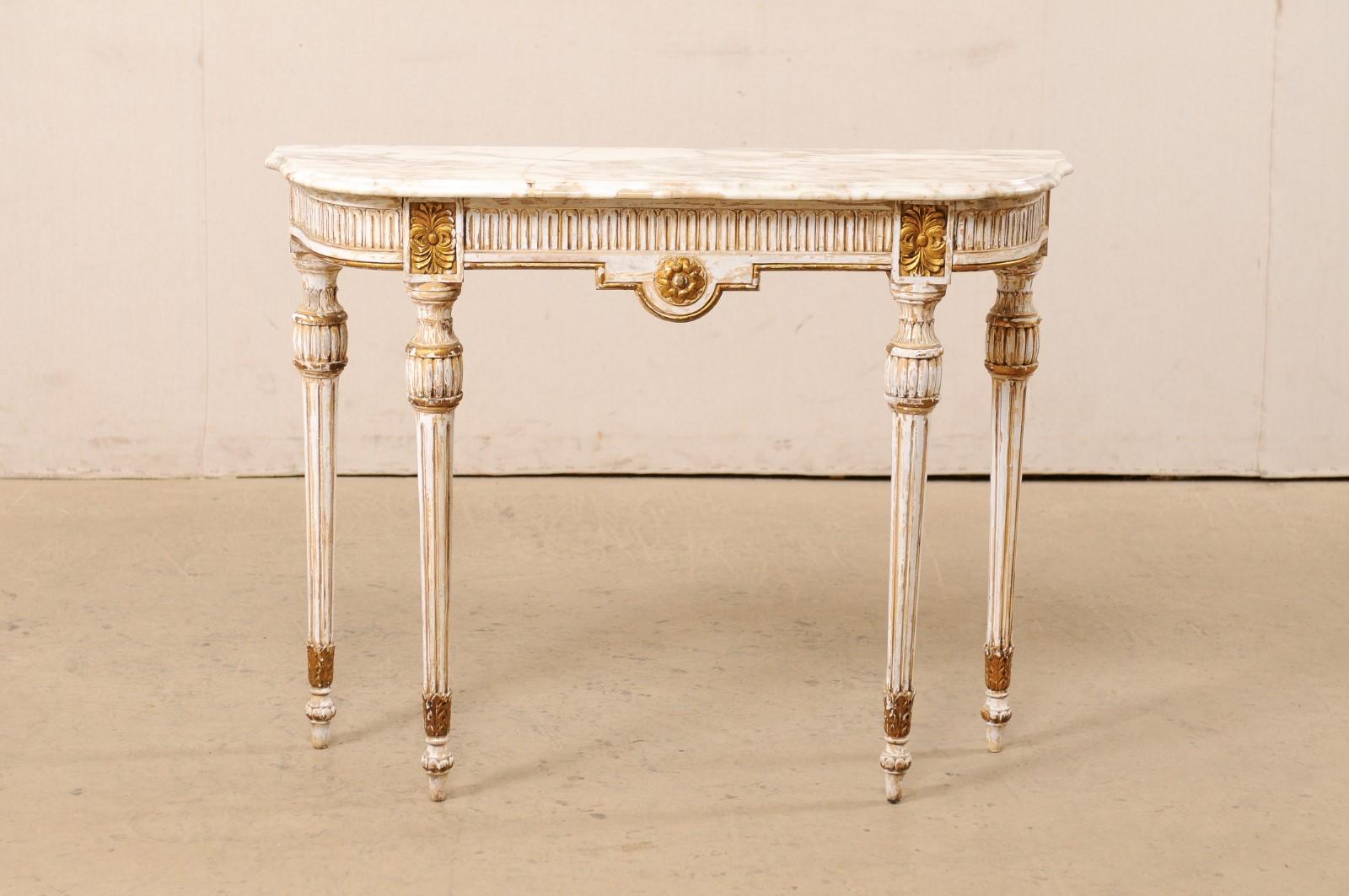 An Italian carved and gilt wood console table with marble top from the mid 20th century. This vintage table from Italy features a marble top that rests upon an apron which is carved with fluted trim along three sides and accented with gilt flower