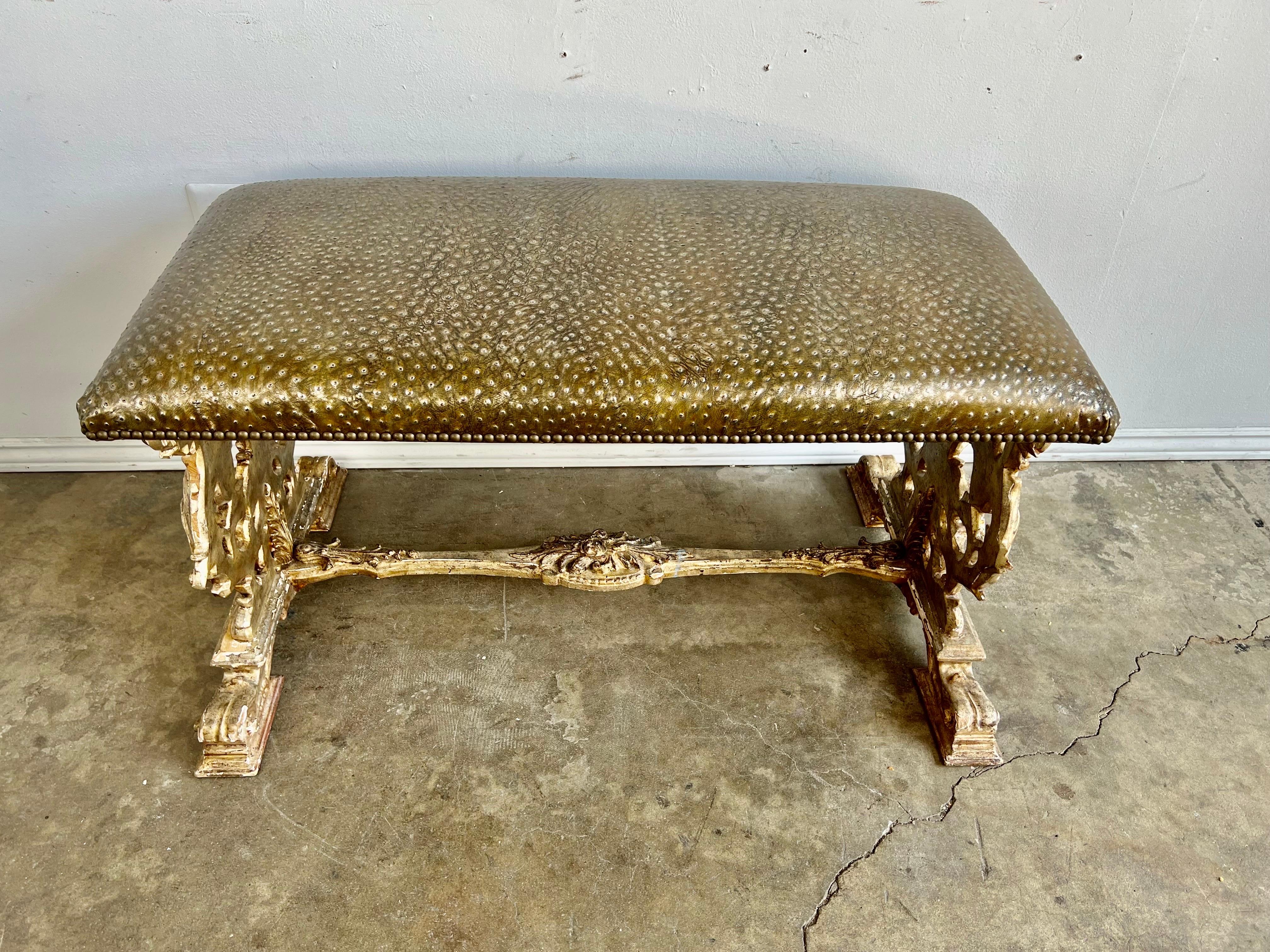 19th C. giltwood Italian Rococo style bench. The bench is beautifully hand carved with details of scrolled acanthus leaves and flowers throughout. The bench is newly upholstered in a bronze colored embossed leather and finished with brass nailhead