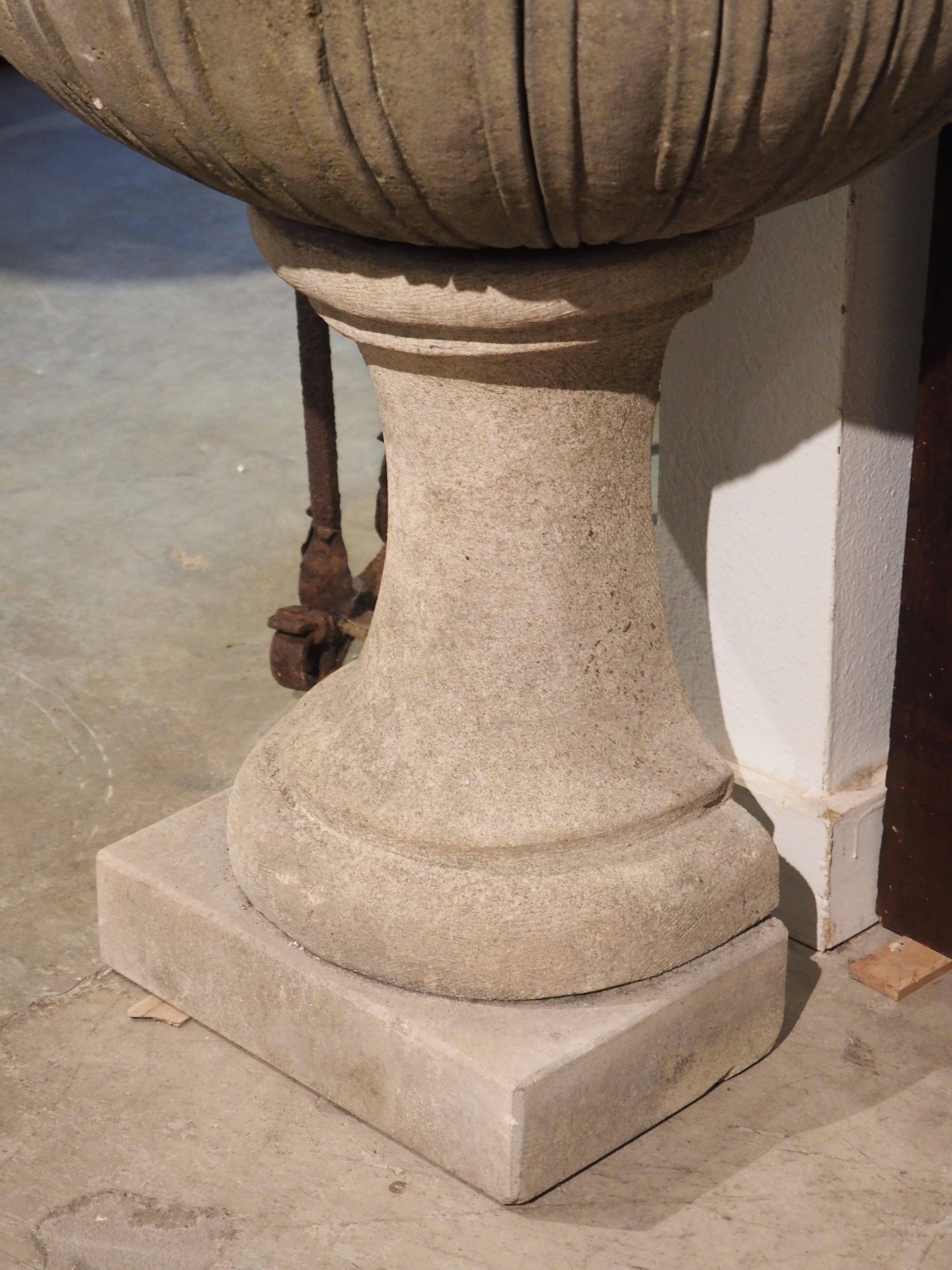 Comprised of three pieces of hand-carved limestone, this Italian wall fountain features a scrolled back wall with a mascaron water feature. All three pieces of stone have a light gray hue but have aged well, with a darkened gray patina mixed with