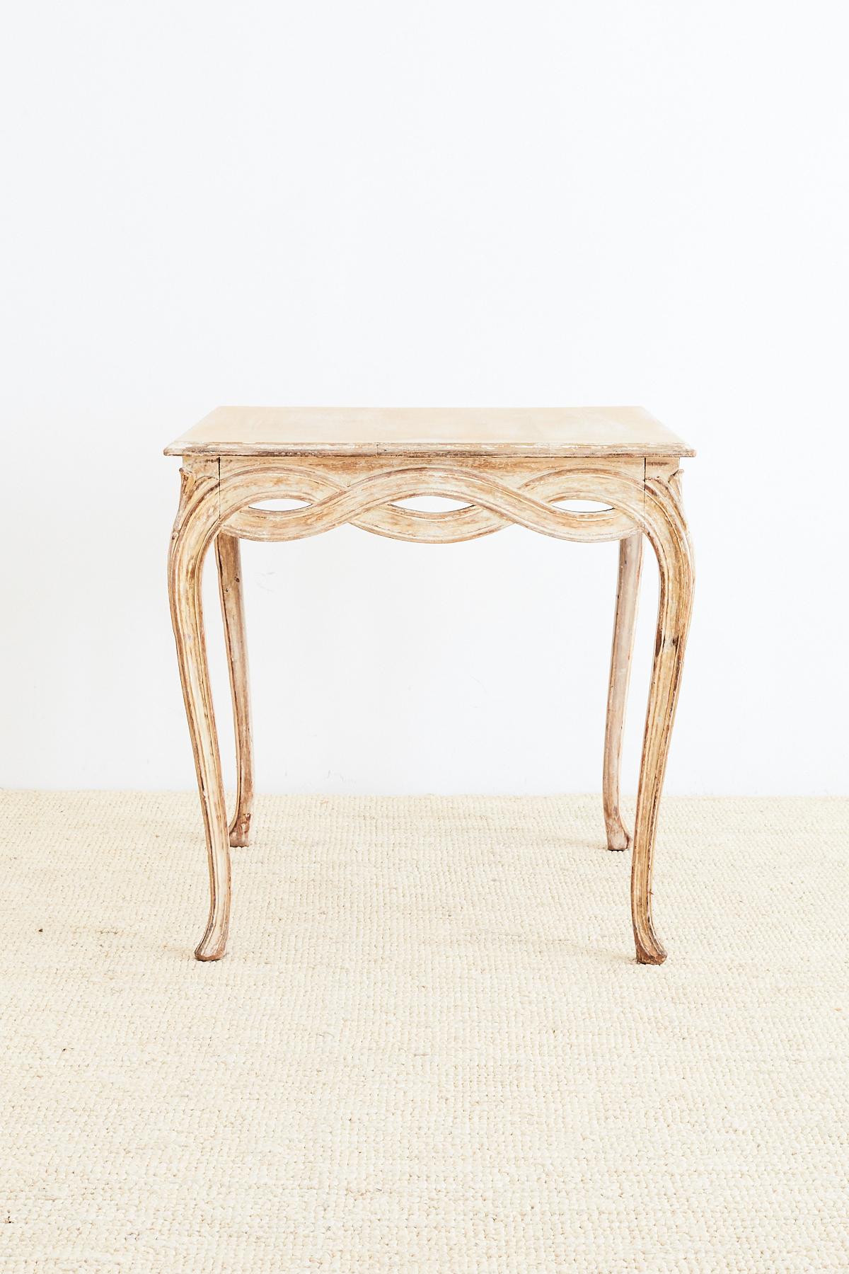 Elegant Italian occasional table or centre table featuring a beautifully carved apron and legs. The tapered cabriole legs intertwine on the apron with a decorative looped design. The table has a distressed or scraped paint finish with lovely old