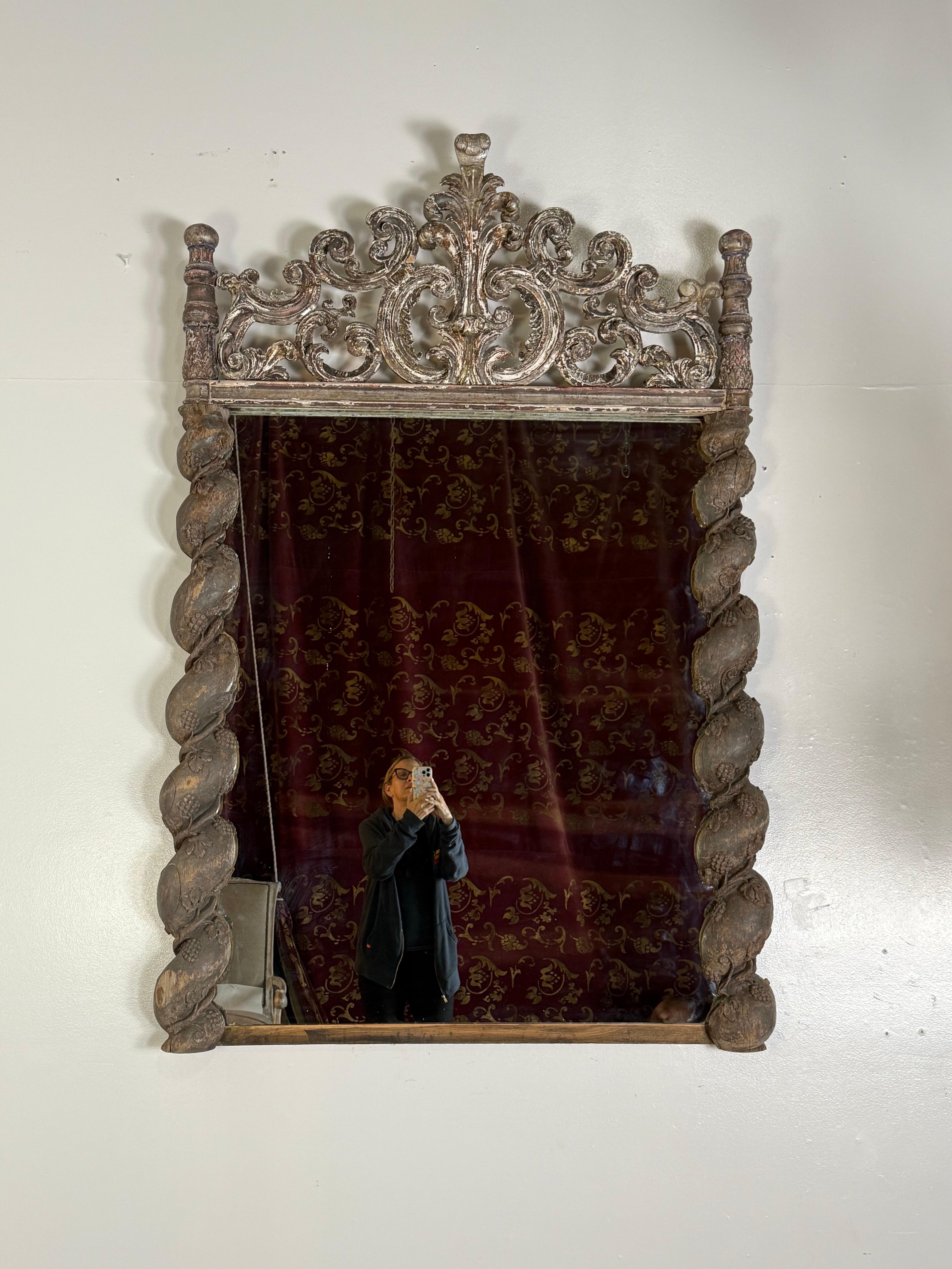 This striking mirror is a bespoke creation crafted using 19th-century elements, showcasing exceptional European craftsmanship and decorative opulence. The top features an elaborate hand-carved crest with scrolling acanthus and floral motifs, richly
